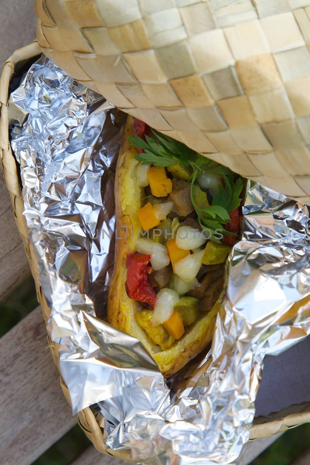 Open-air lunch for a vegetarian- potato baked with vegetables and cheese in an aluminium foil. Dish is hidden in the woven birch basket