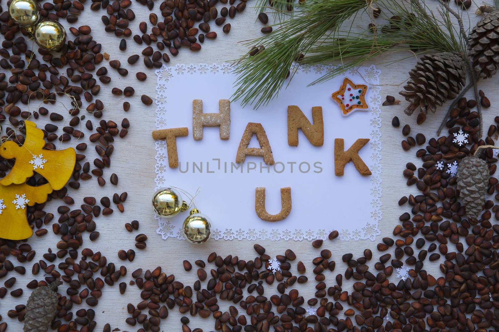 Winter holidays cedar nuts background on a wooden surface with  biscuits inscription:"Thank u"