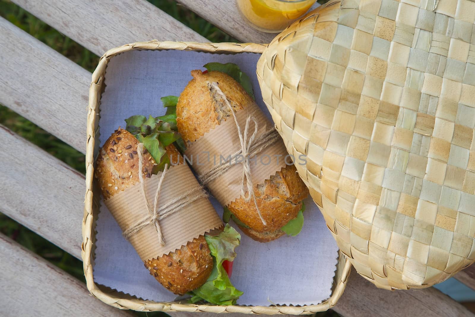 An open-air  express lunch for a vegetarian- whole grain rolls with fresh vegetables and a glass of fresh orange juice. Rolls are hidden in the woven birch basket