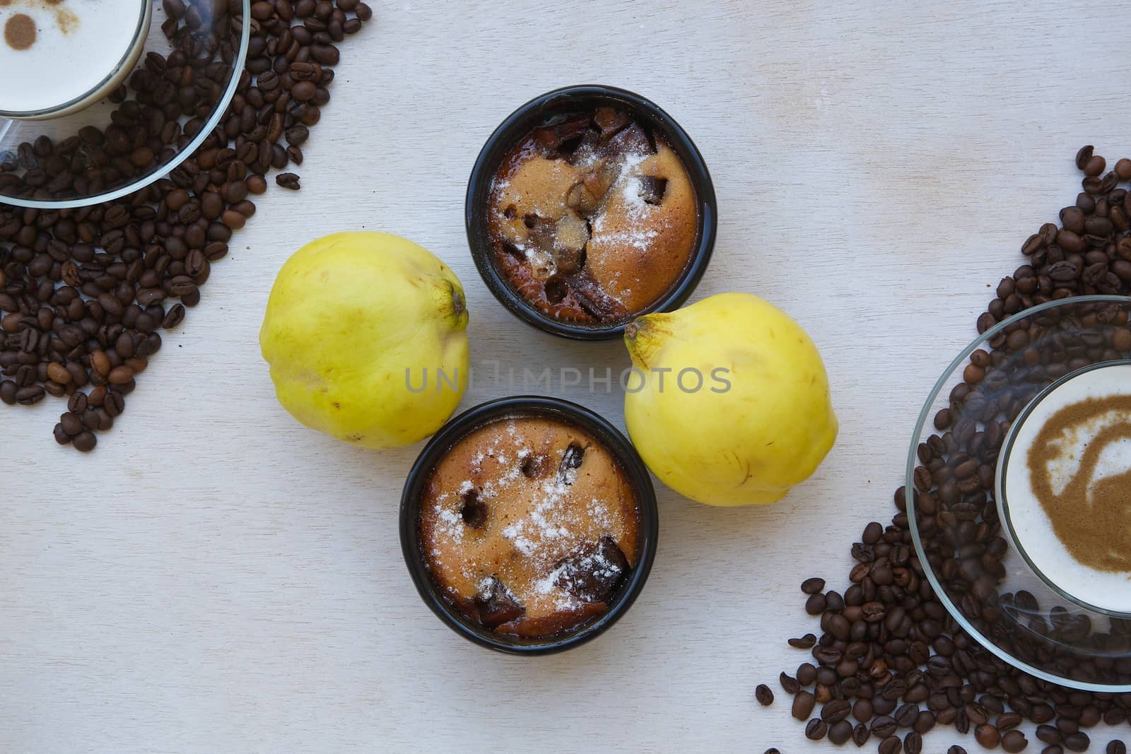 Small quince pies in black ceramic moulds, two fresh quinces, two glass cup of cappuccino. Top view