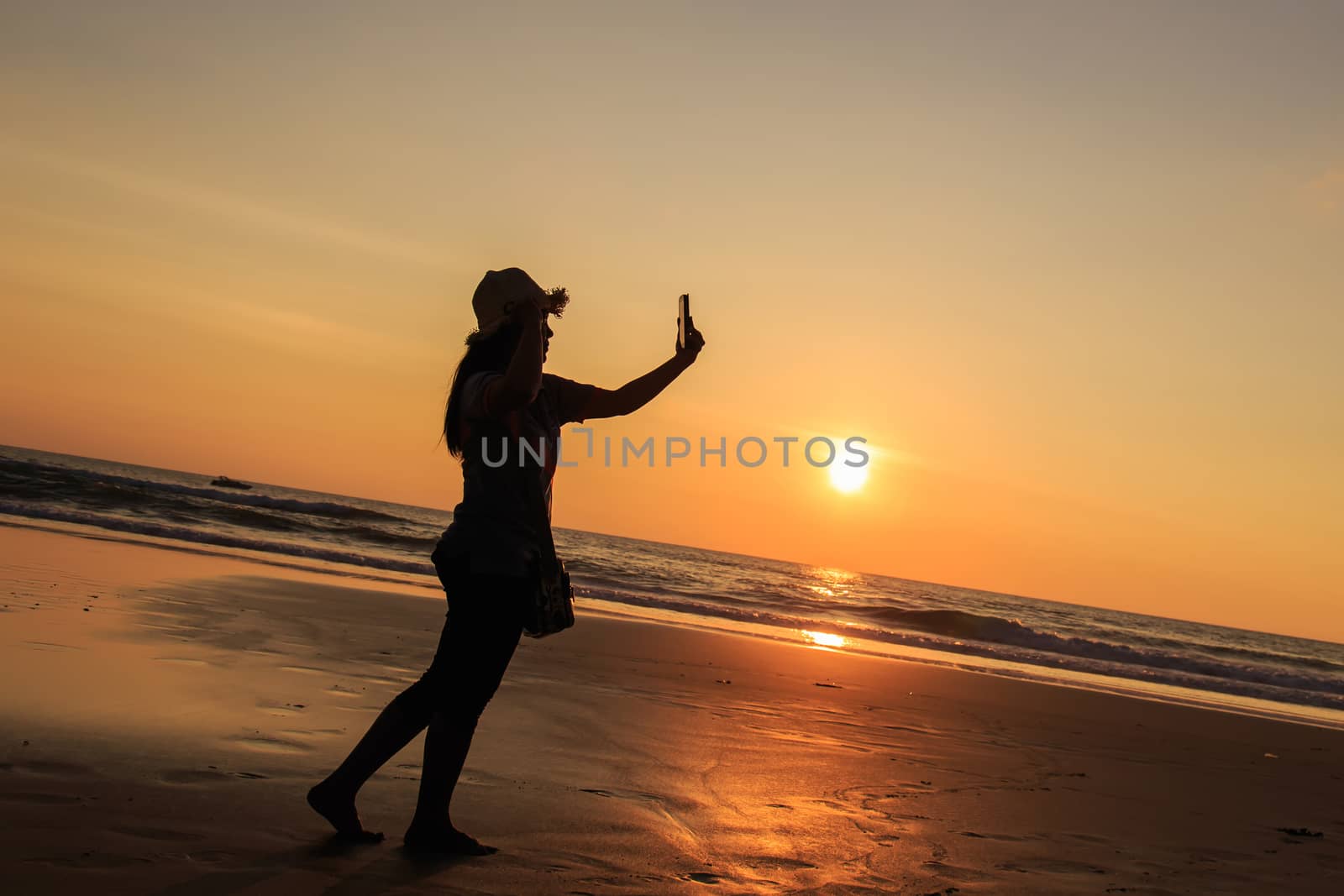 Silhouette of Thai Woman using smartphone at the beach in sunset by nanDphanuwat