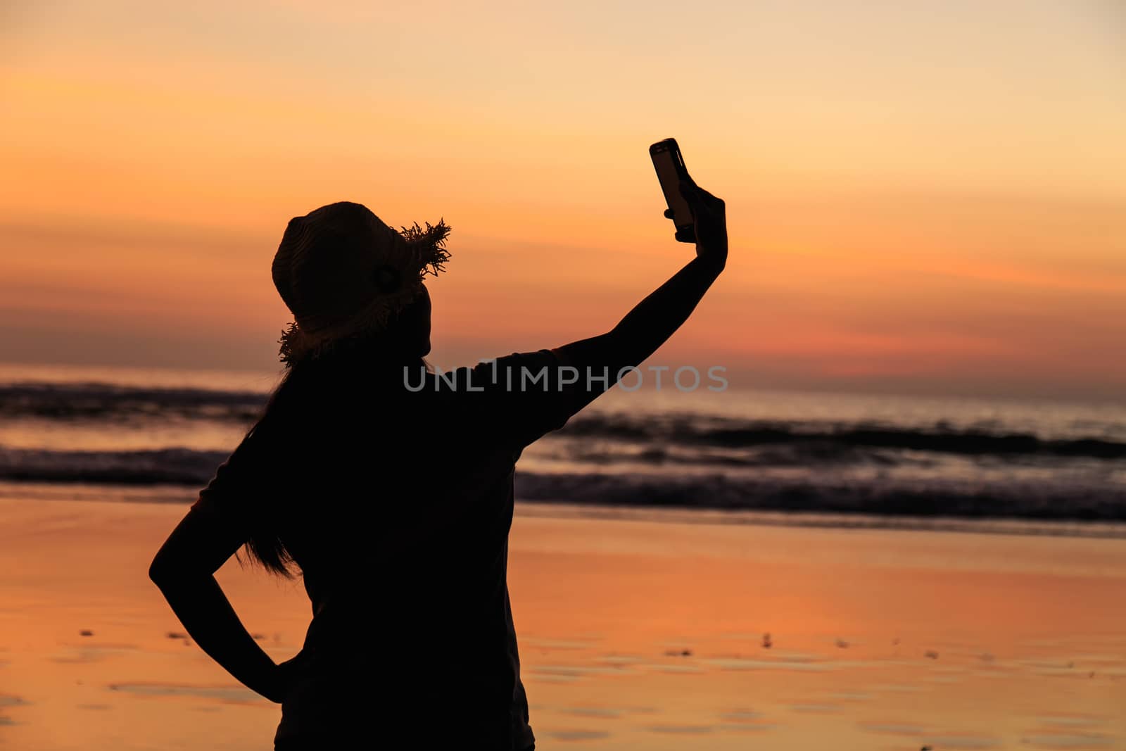 Silhouette of Thai Woman using smartphone at the beach in sunset by nanDphanuwat