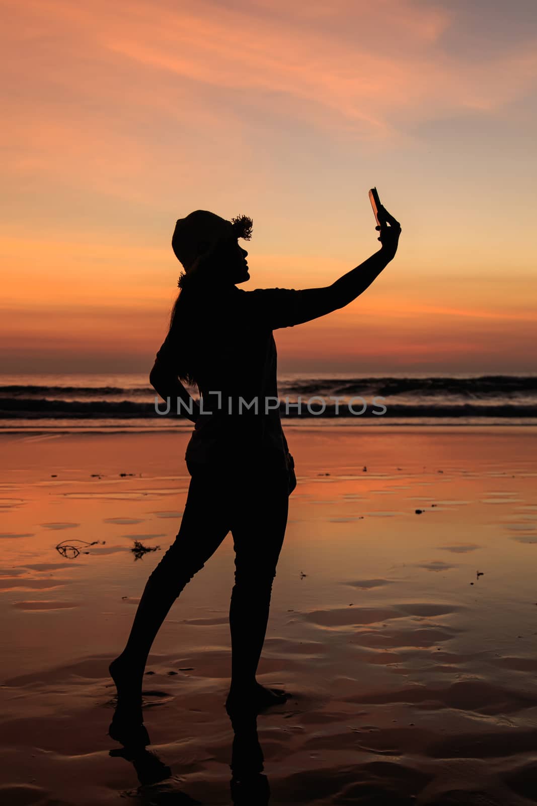 Silhouette of Thai Woman using smartphone at the beach in sunset time