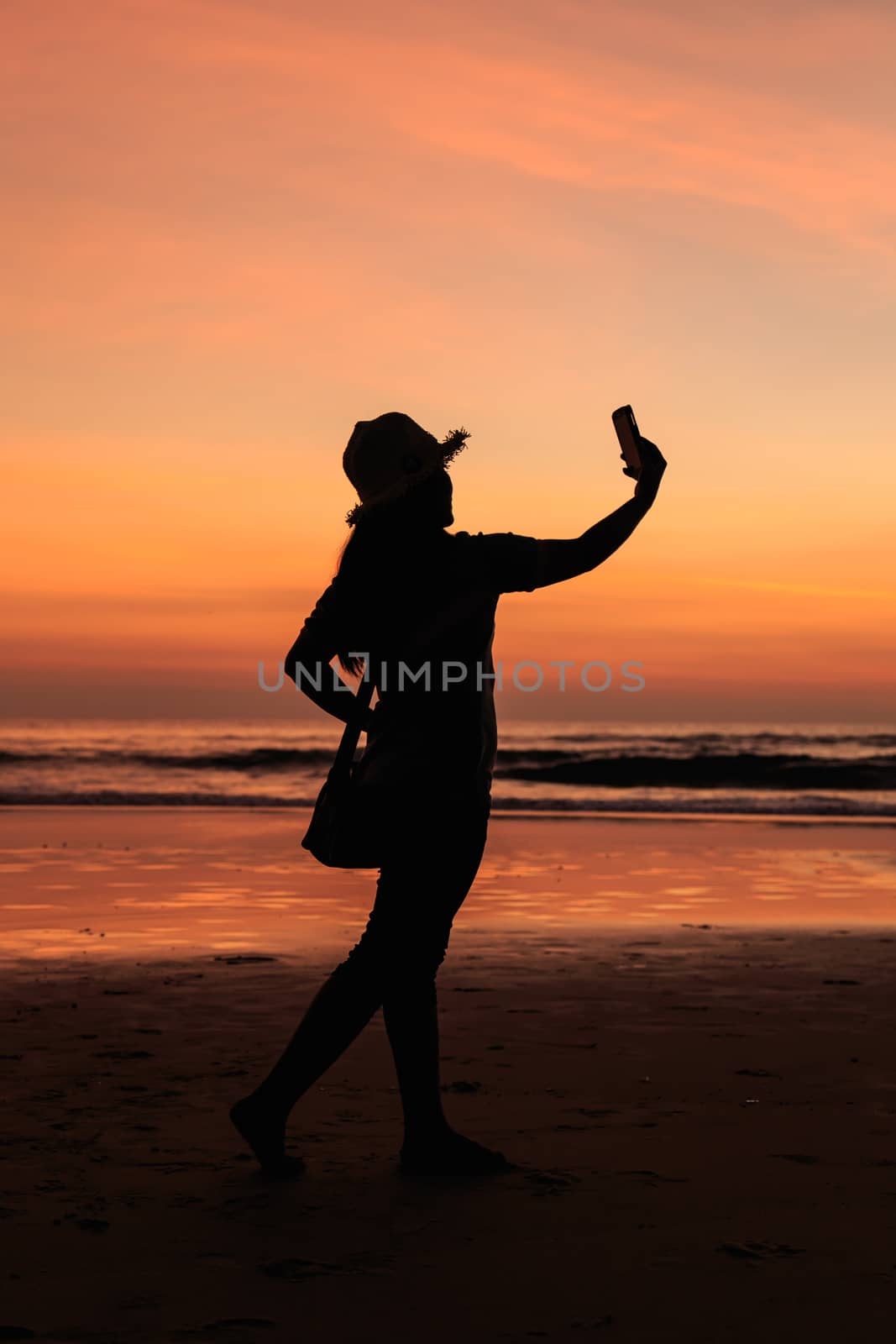 Silhouette of Thai Woman using smartphone at the beach in sunset by nanDphanuwat