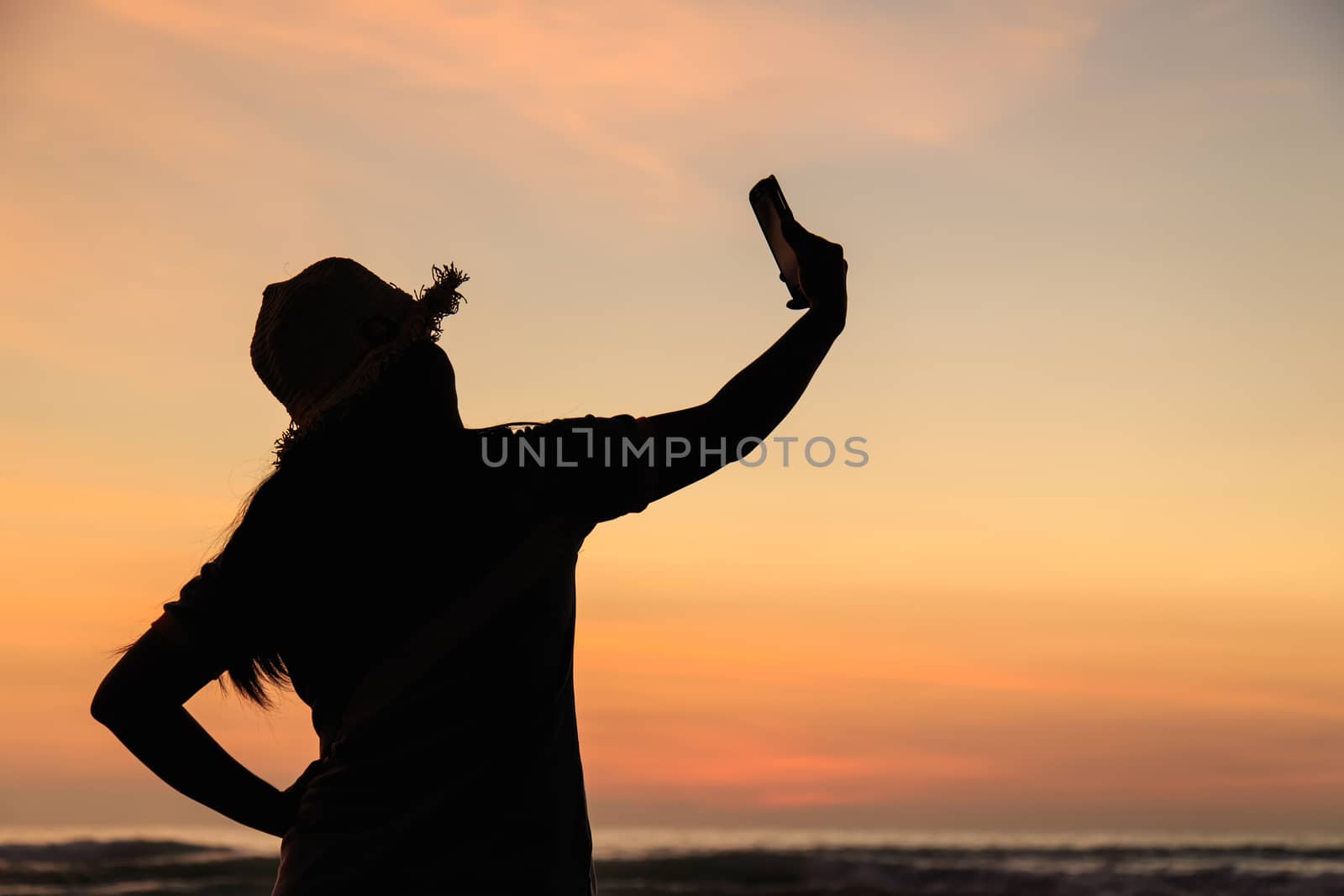 Silhouette of Thai Woman using smartphone at the beach in sunset by nanDphanuwat