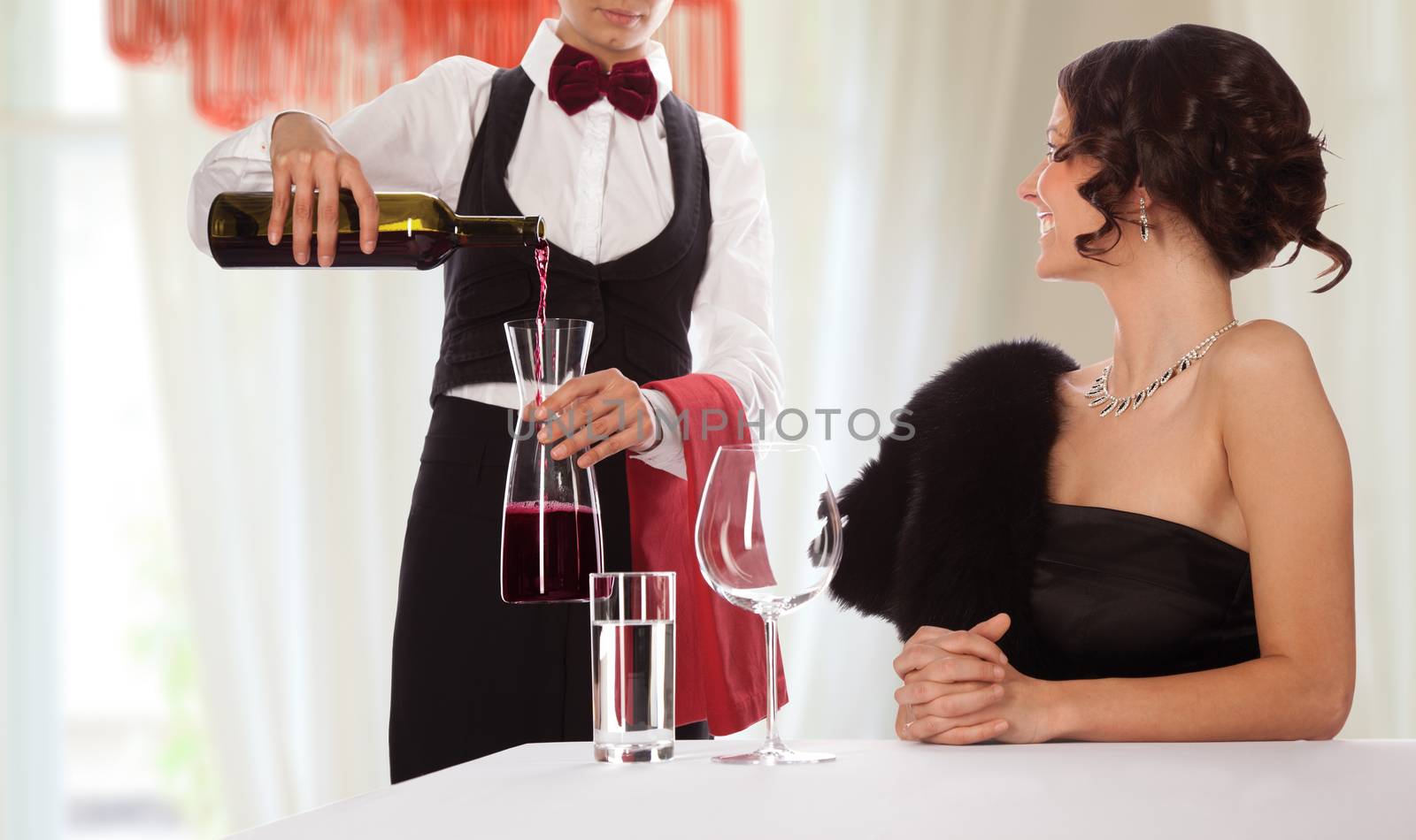 Waitress serving wine to a smiling lady guest. Isolated with work path