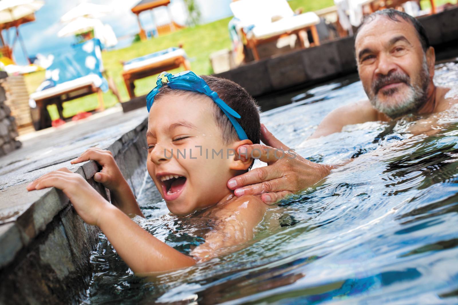 grandfather playing with his grandson in an outdoor pool.