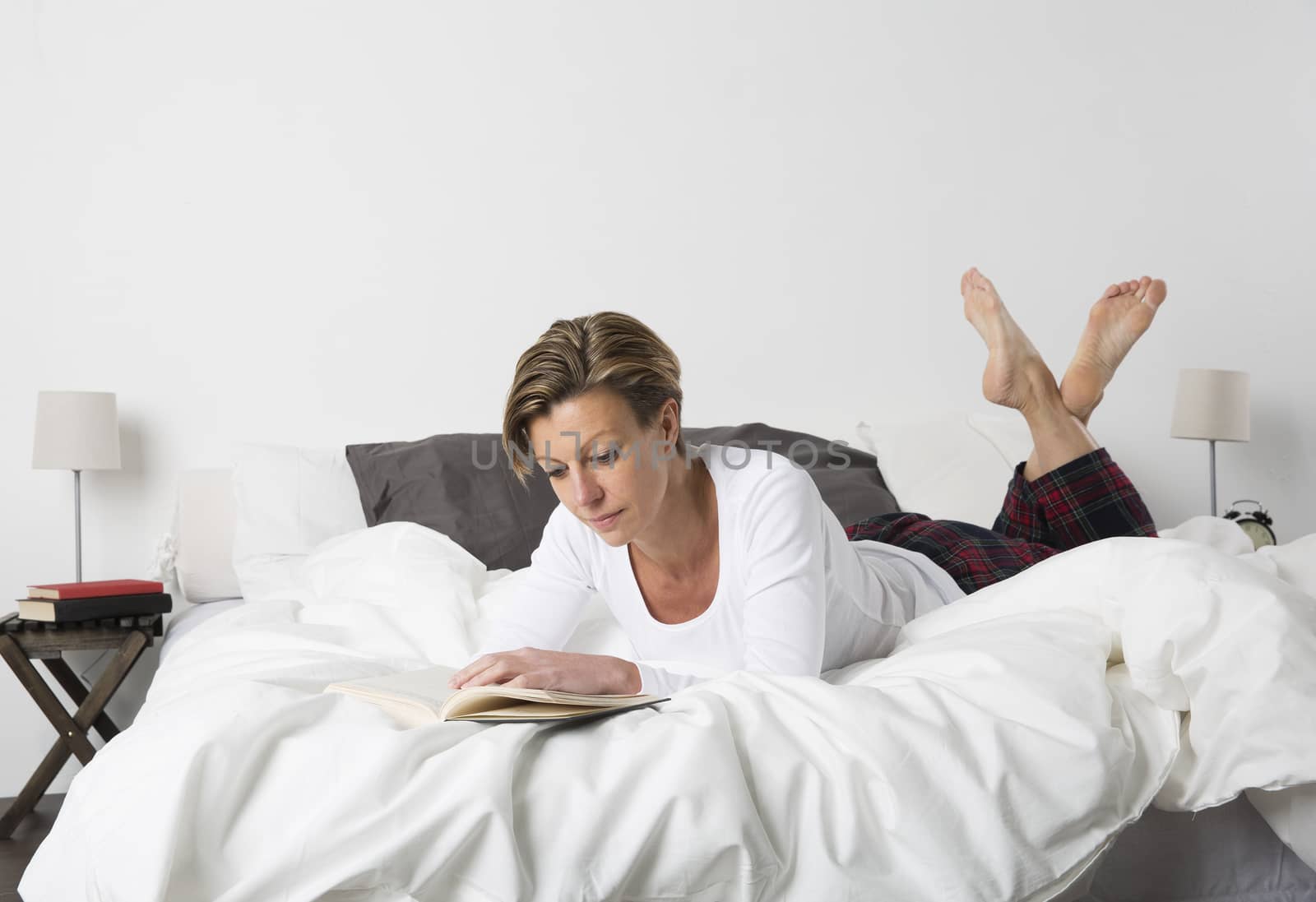 Adult woman with short hair reading a book in bed