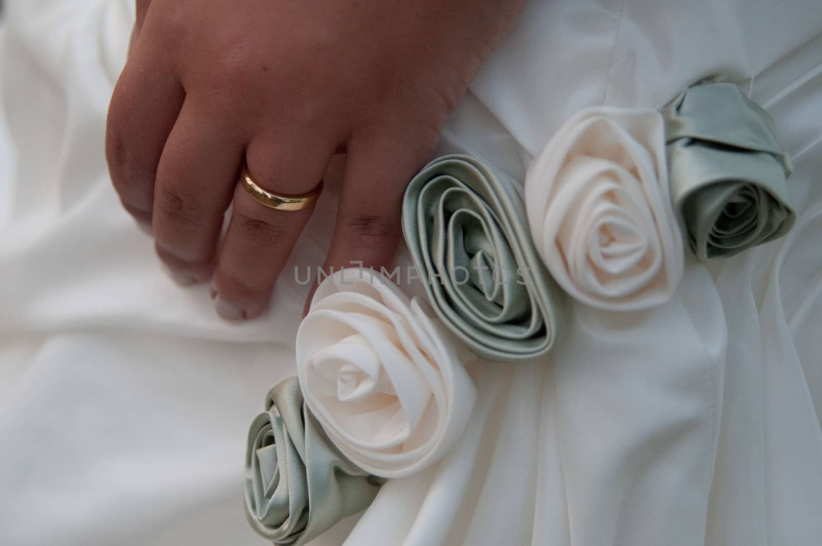 Bride keeps hand with wedding ring close to rose decoration on her dress by Mag6619