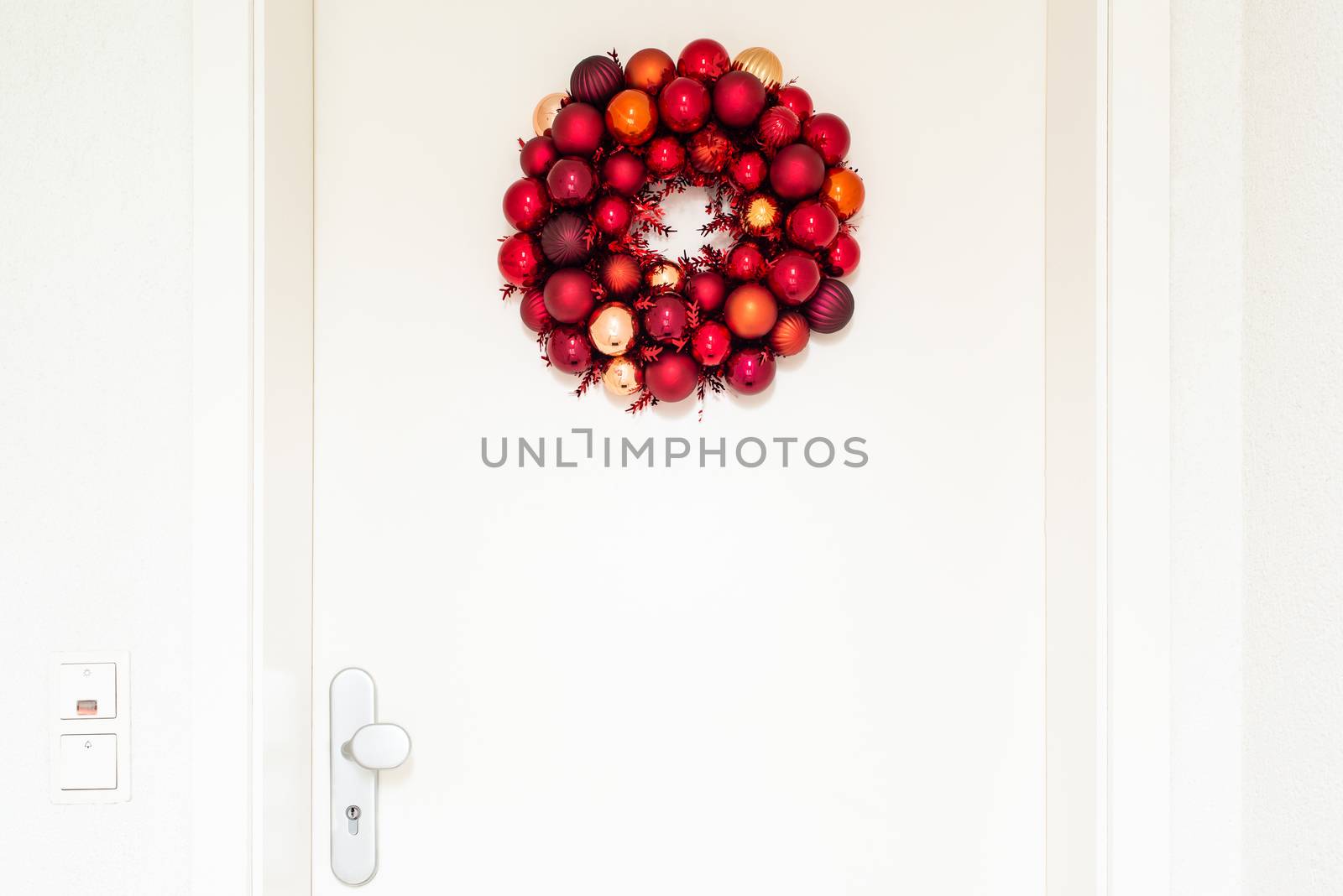 Christmas wreath decorated with red balls on white entrance door to a flat