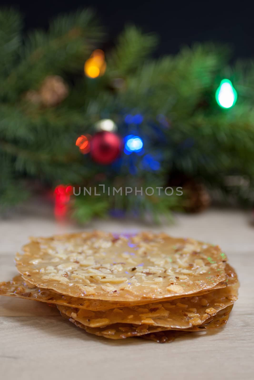 Lace cookies on a table with Christmas tree branches in the background.