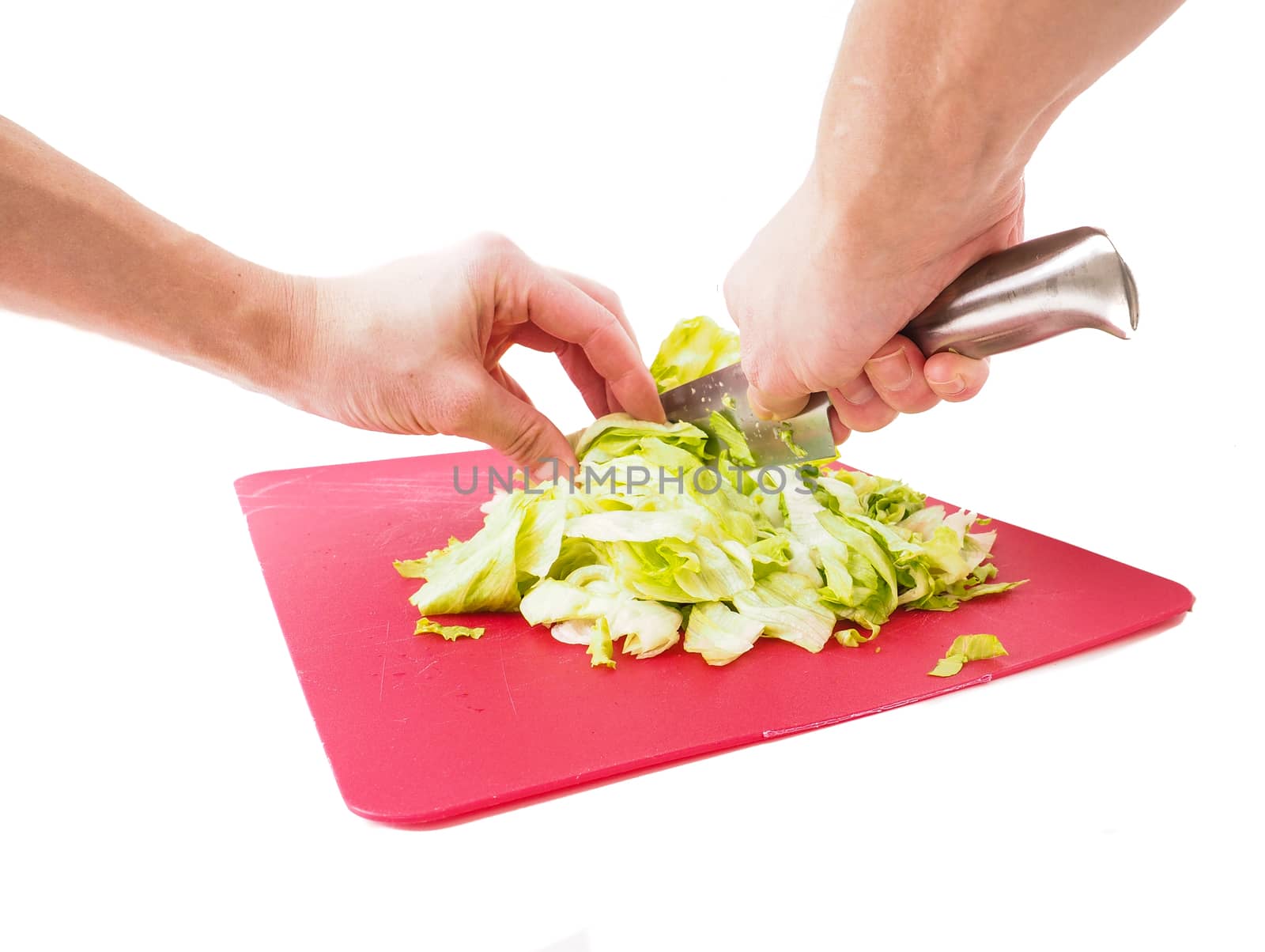 Hands cutting fresh green lettuce salad with grey metal knife on red plastic cutting board towards white