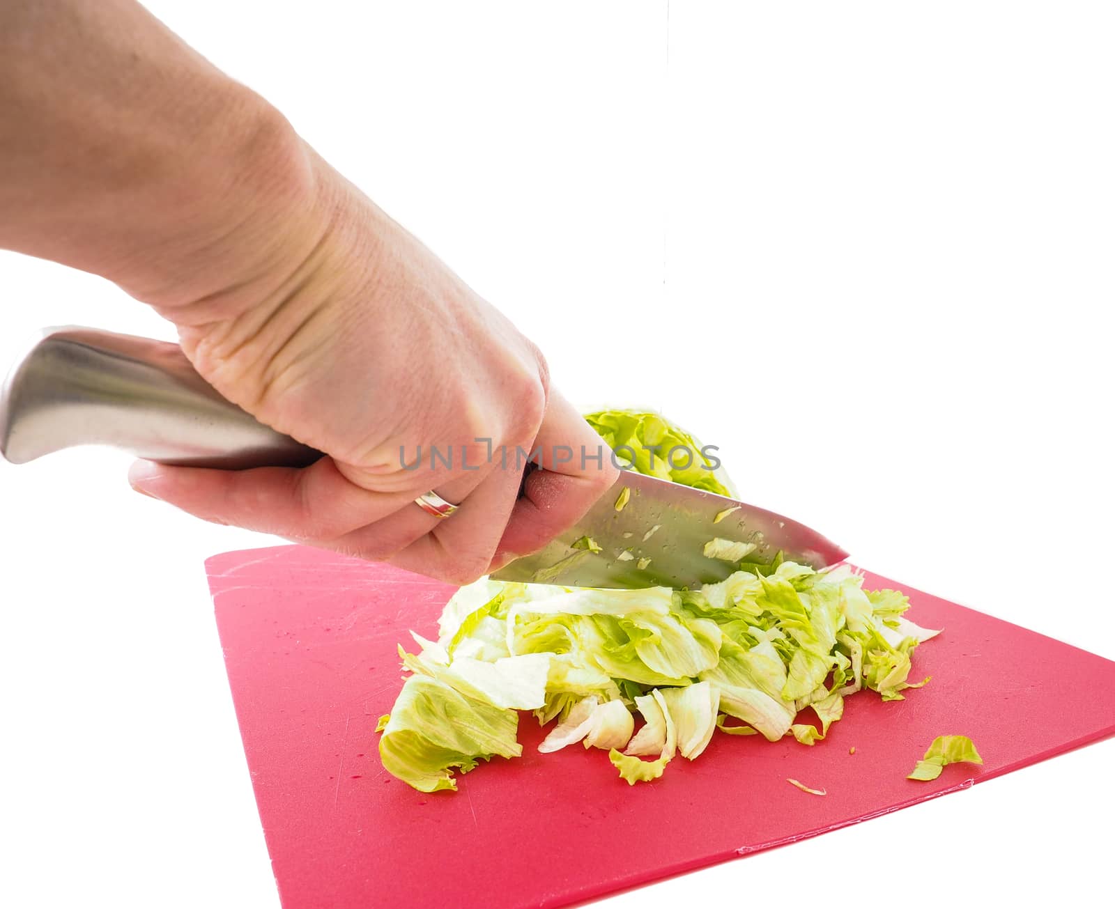 Hand cutting fresh green lettuce salad with grey metal knife on red plastic cutting board towards white