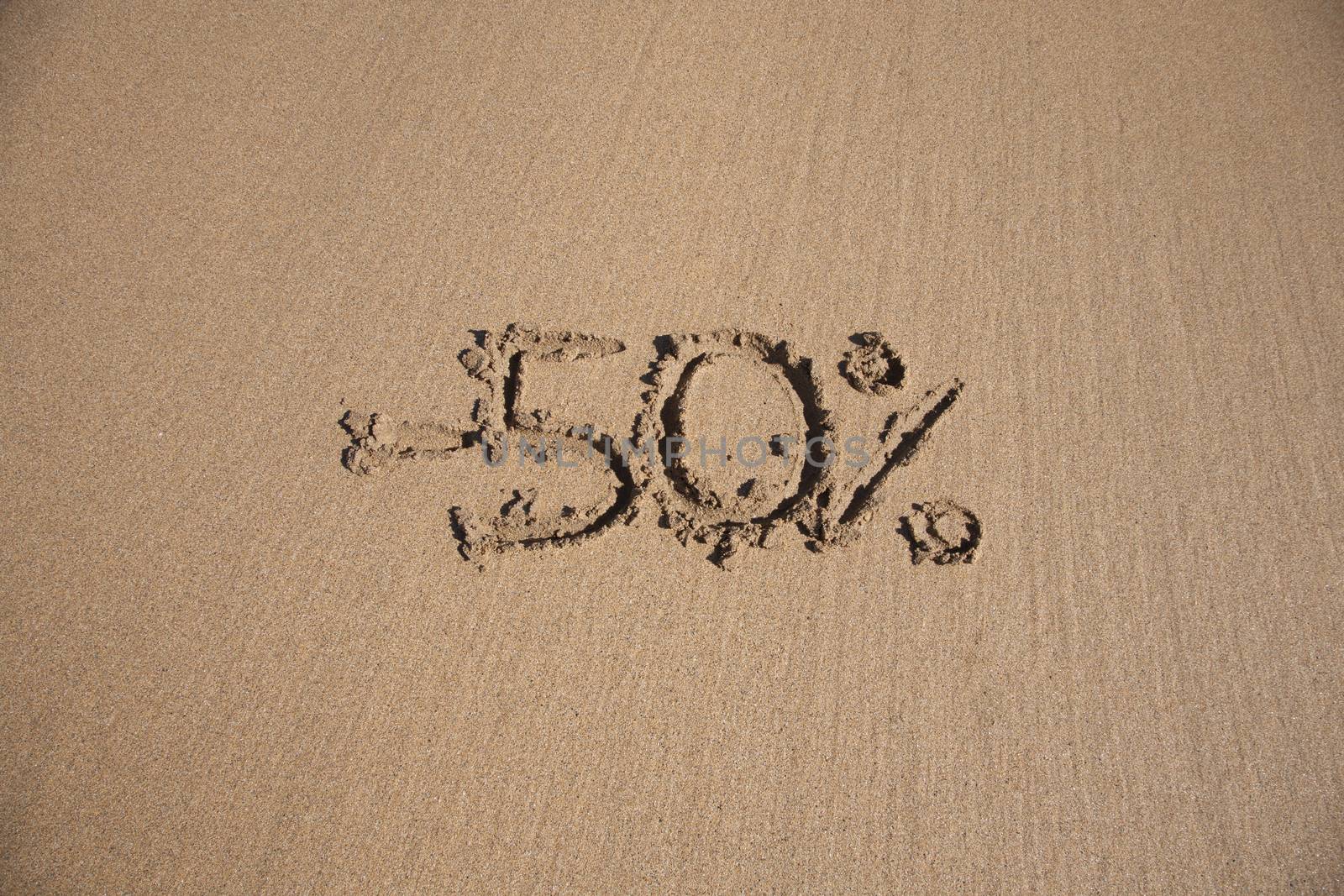 50 percent discount in earth text written on brown sand ground low tide beach ocean seashore in Spain Europe
