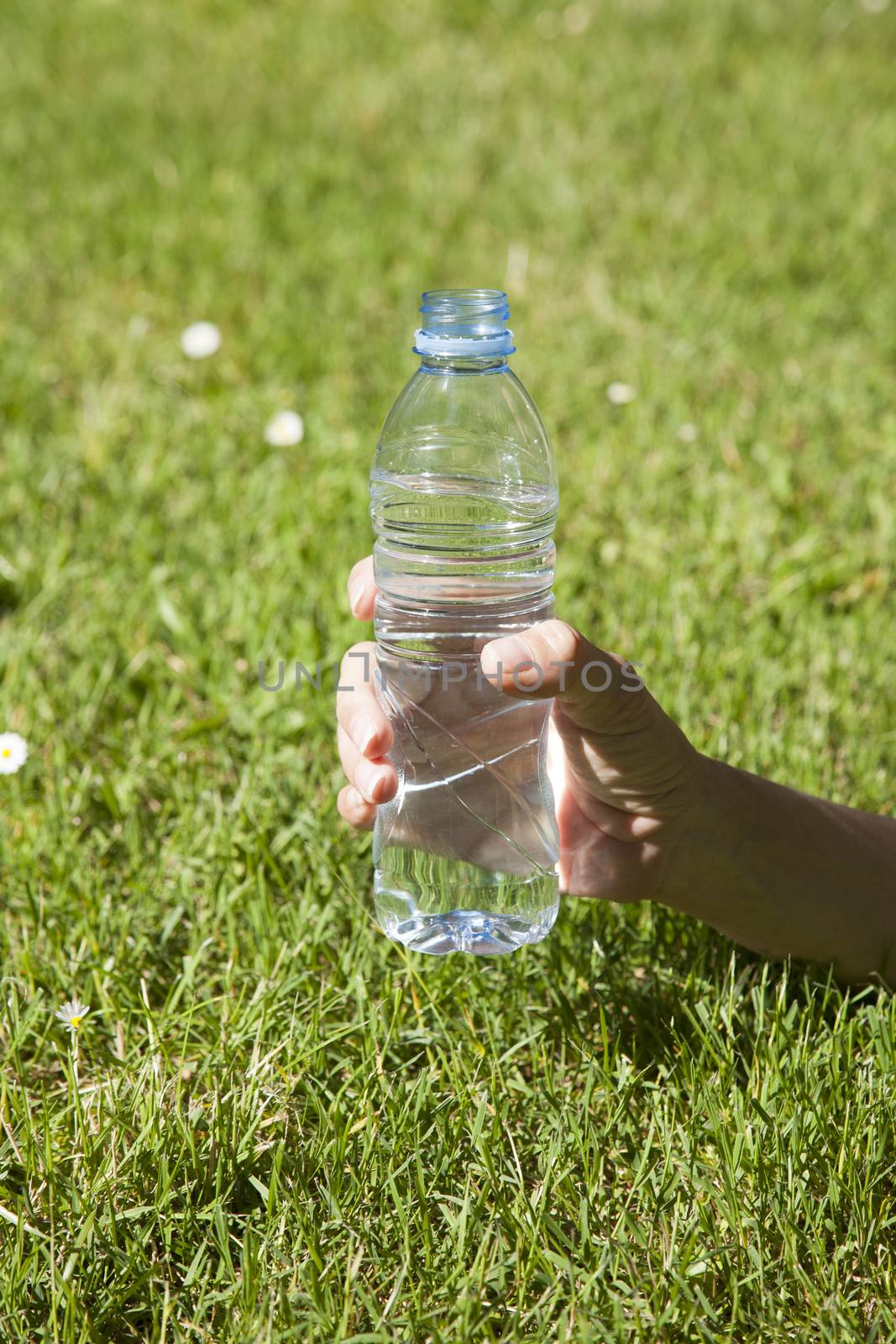 transparent small plastic water bottle with blue cap in woman hand on green lawn outdoor