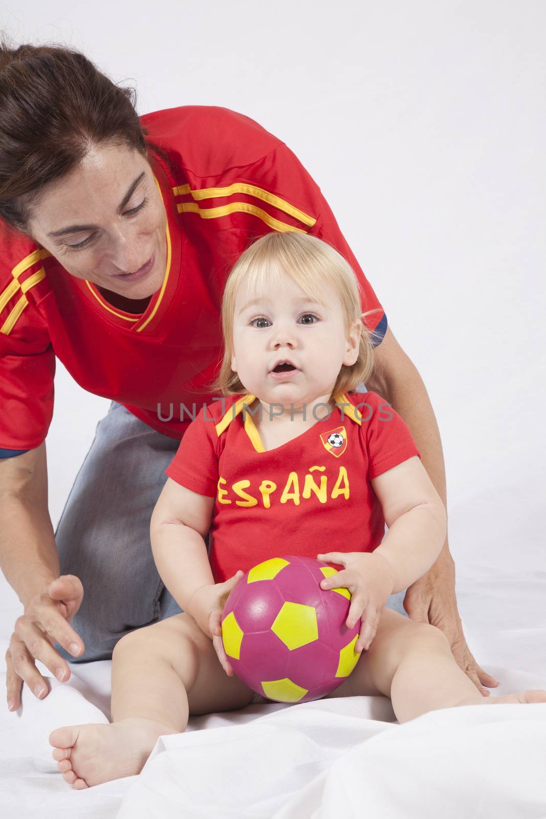 surprised face blonde baby sixteen month old with red shirt of Spanish soccer team and mother