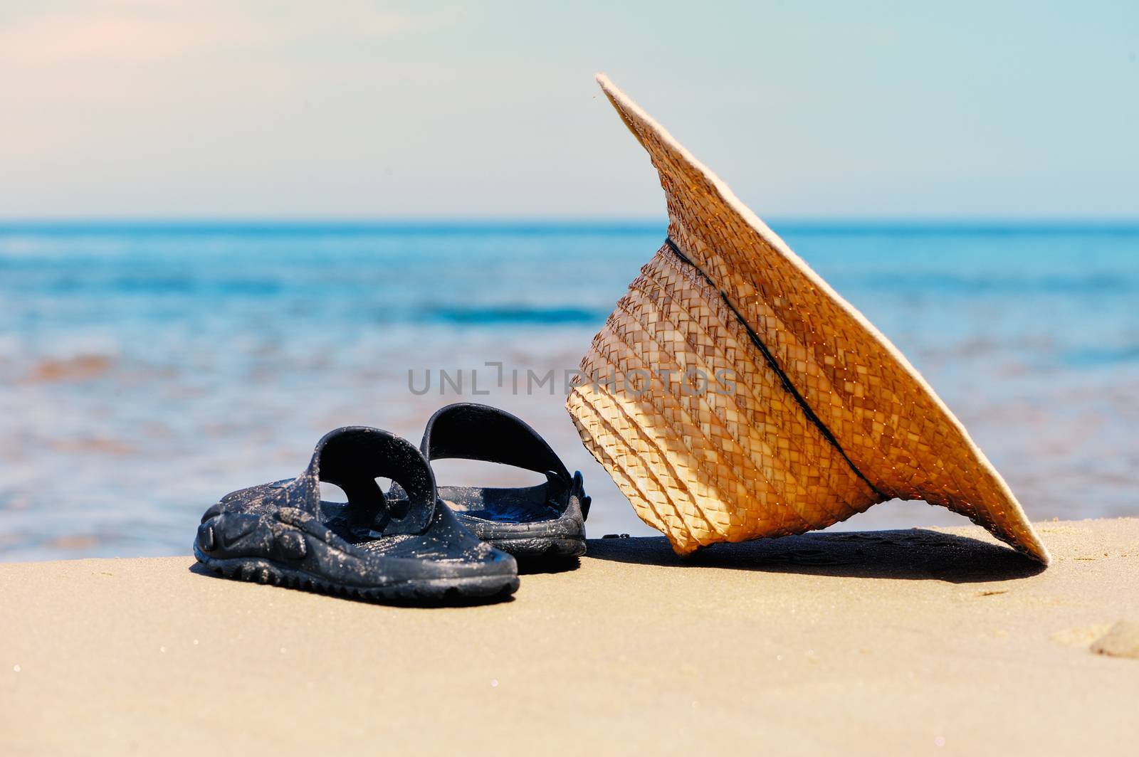 Wicker hat and rubber sandals on the sandy beach