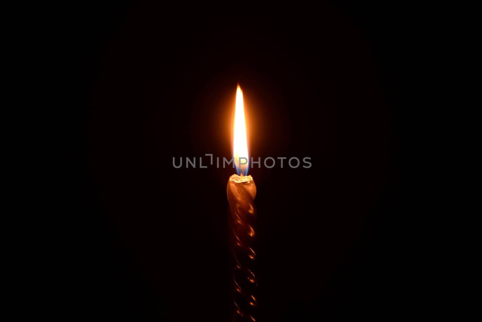 Photo of a golden candle burning on a black background.