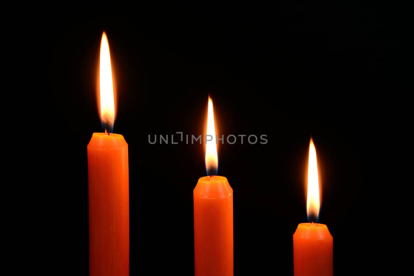 Photo of three orange candles burning on a black background.