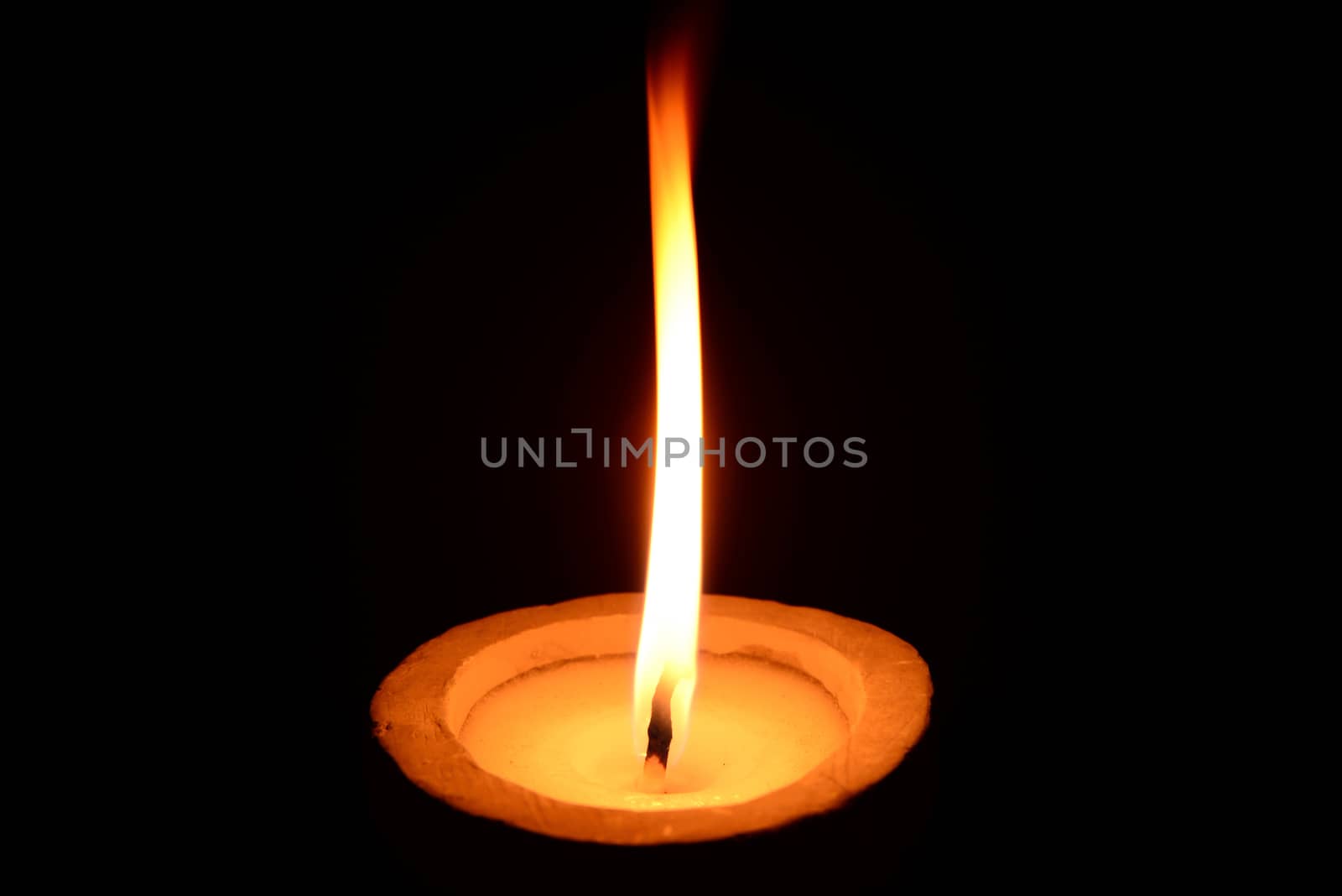 Photo of a white candle with stone candlestick burning on a black background.