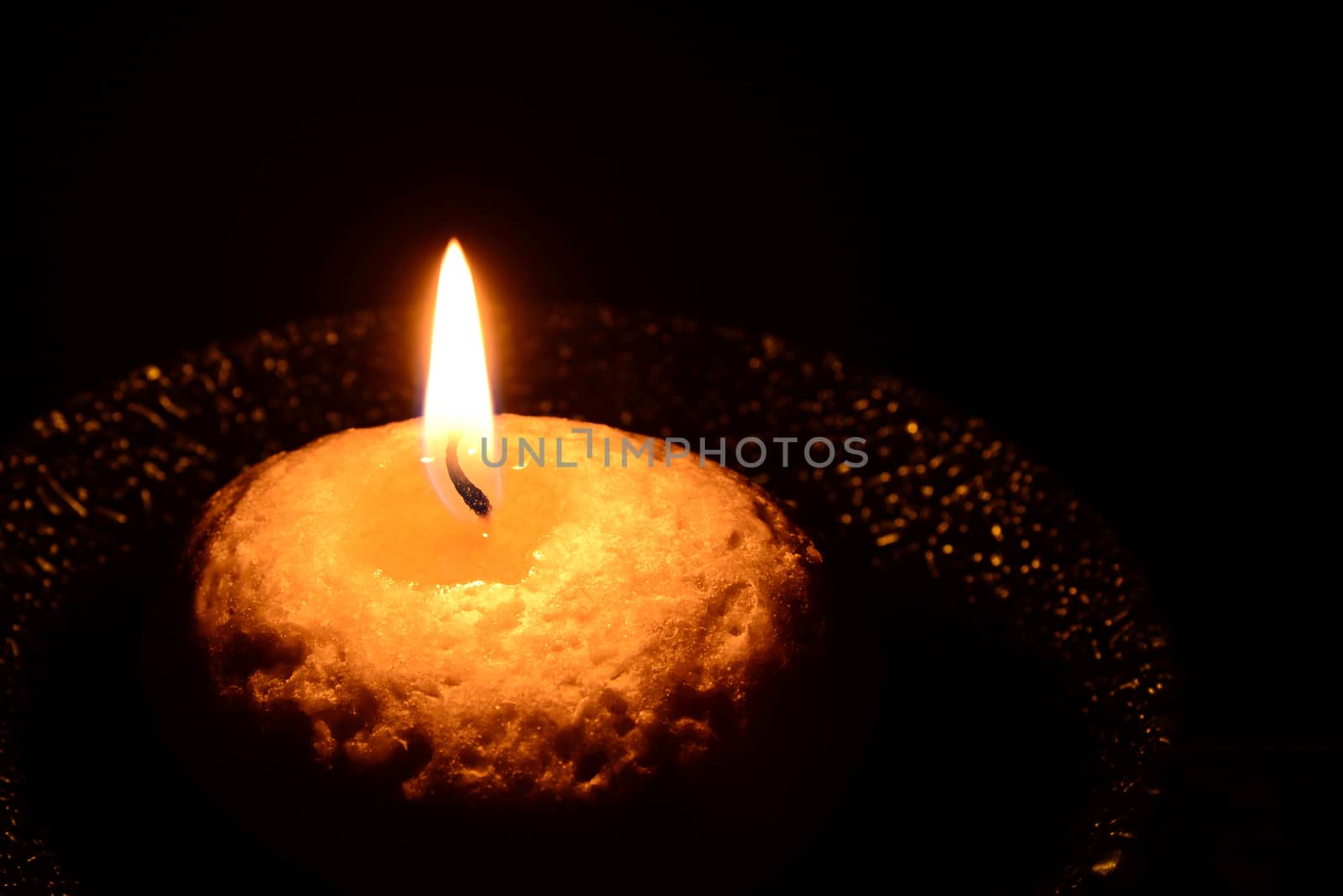 Photo of a white candle on a green plate burning on a black background.