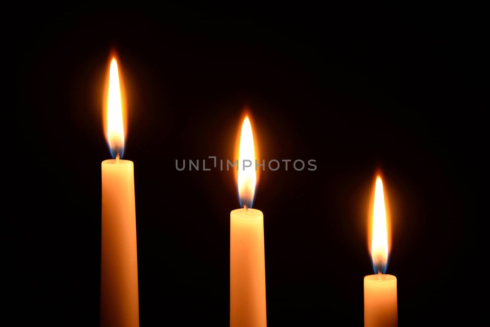 Photo of three white candles burning on a black background.