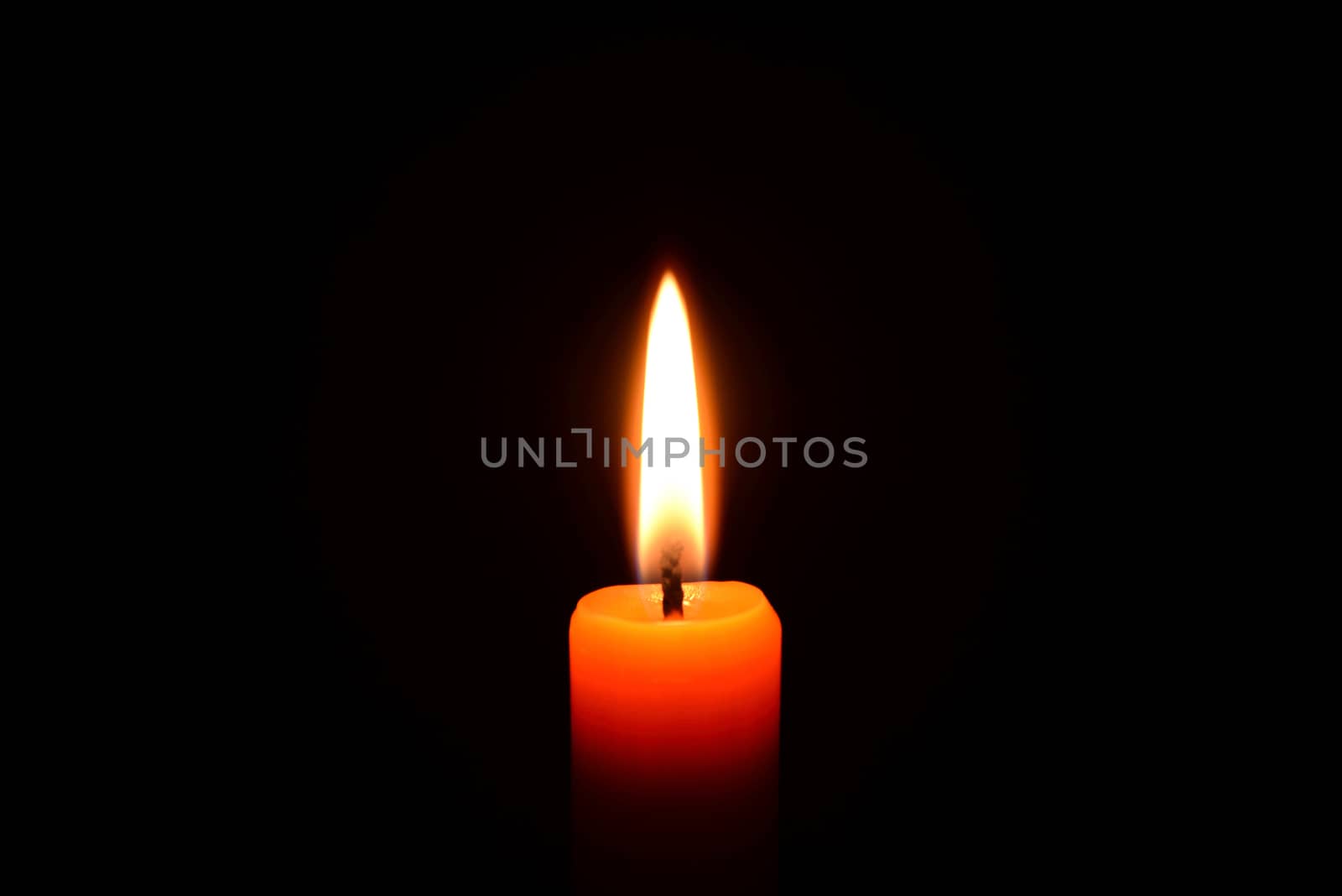 Photo of an orange candle burning on a black background.