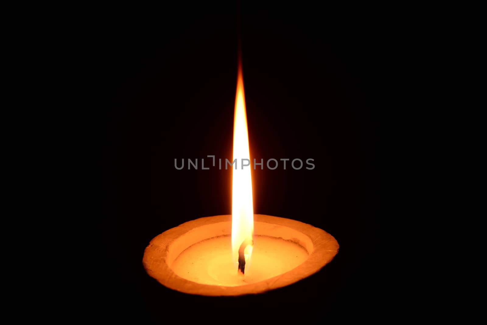 Photo of a white candle with stone candlestick burning on a black background.