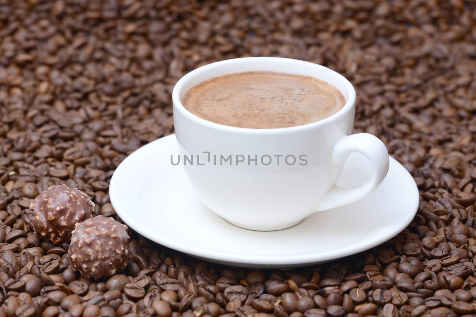 Photo of a cup of coffee on a saucer with candies. White color cup on a brown coffee beans background. Food photography.