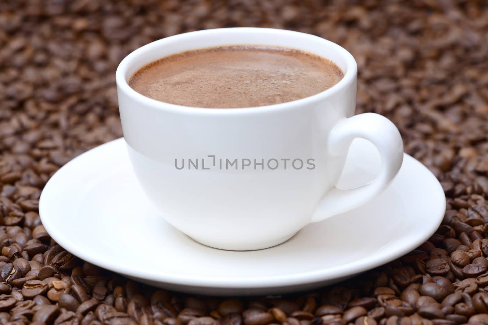 Photo of a cup of coffee with on a saucer. White color cup on a brown coffee beans background. Food photography.