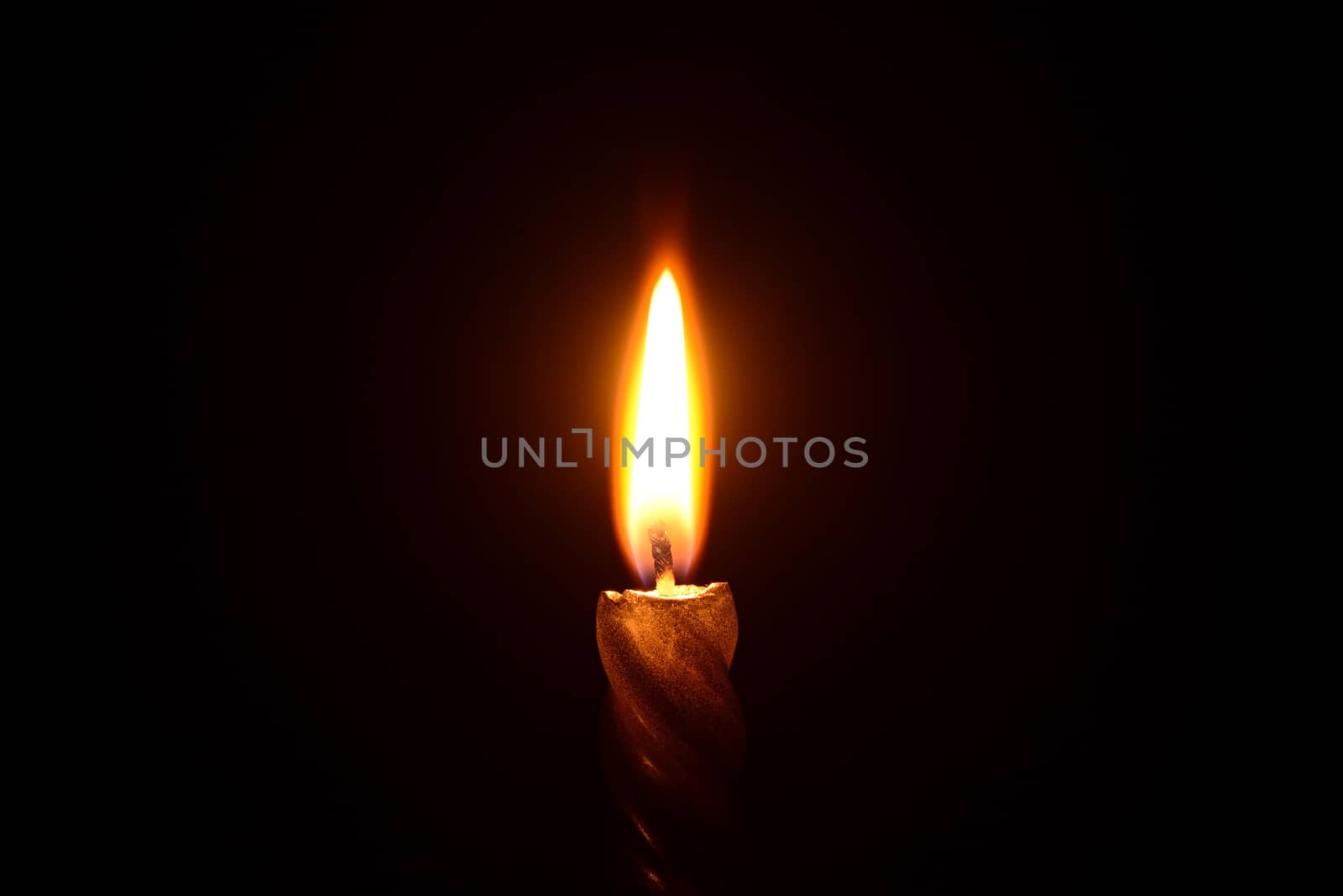 Photo of a golden candle burning on a black background.