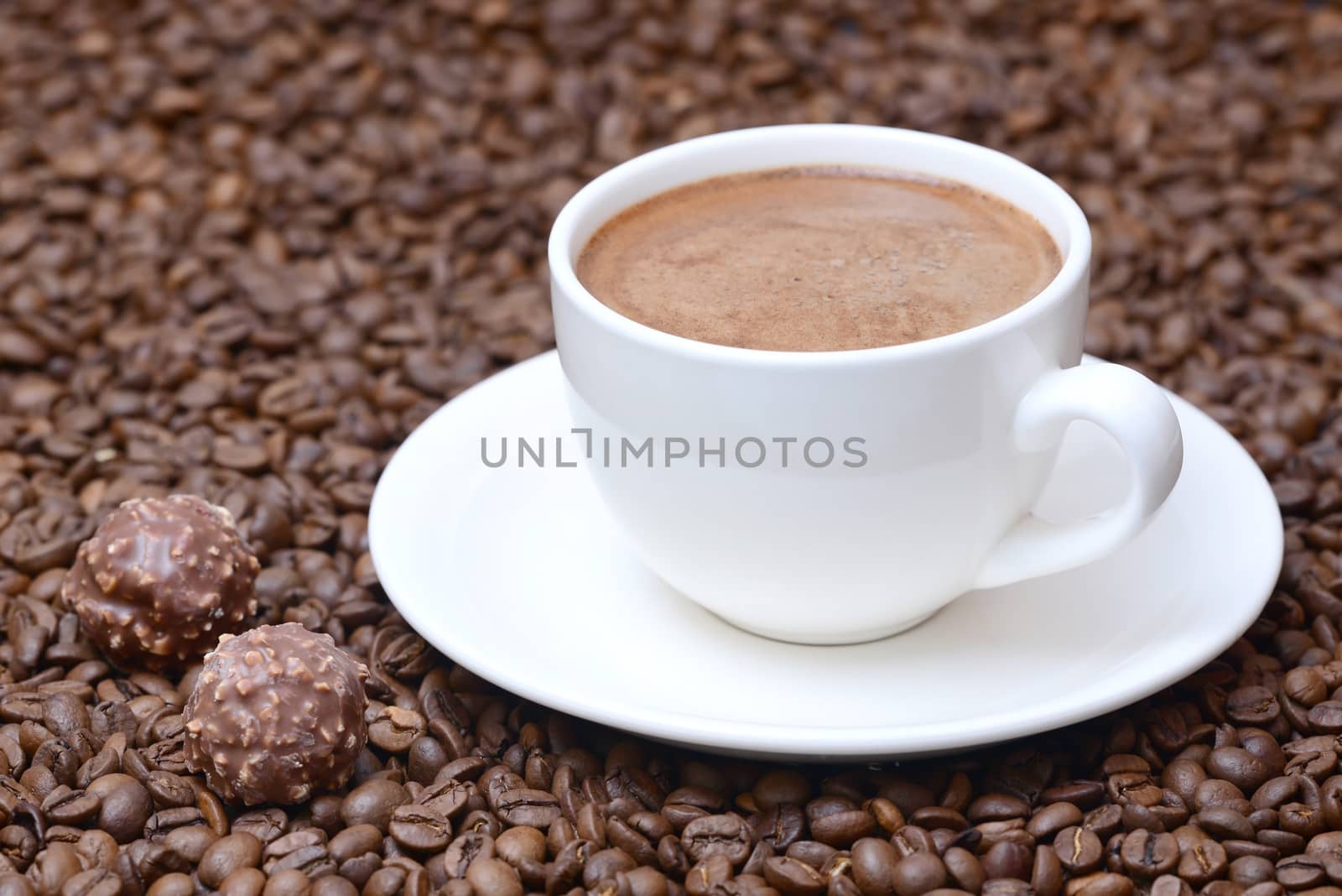 Photo of a cup of coffee on a saucer with candies. White color cup on a brown coffee beans background. Food photography.