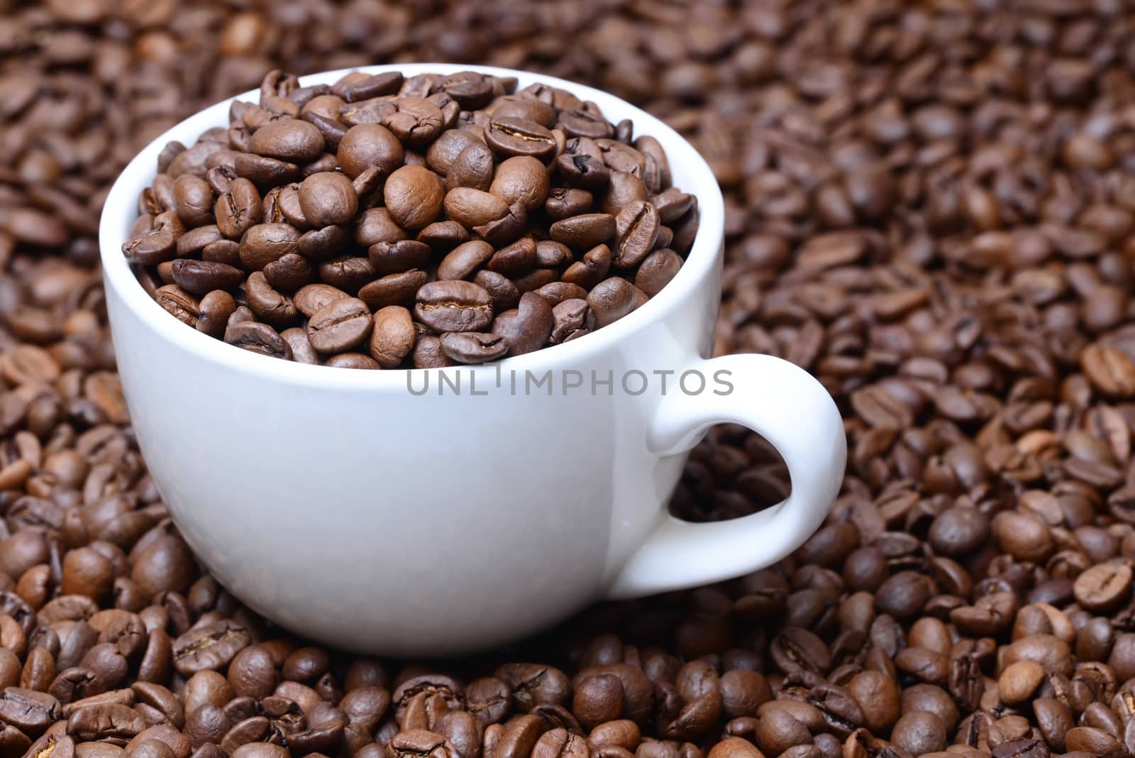 Photo of a cup of coffee with coffee grains. White color cup on a brown coffee beans background. Food photography.