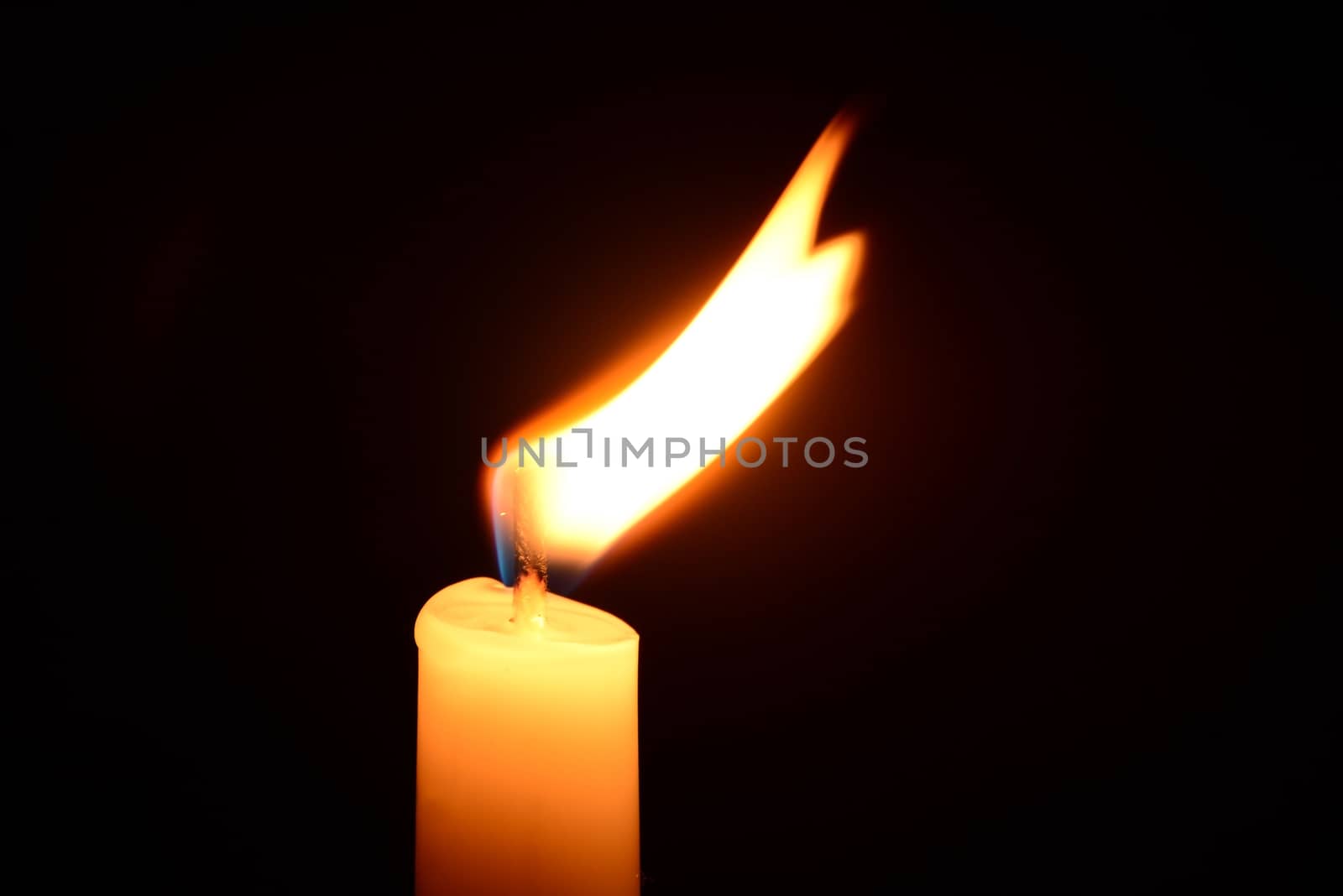 Photo of a white candle burning on a black background. Objects photography.