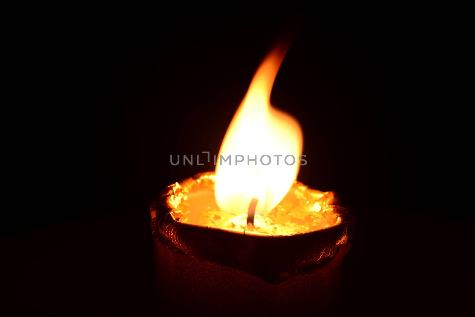 Photo of a golden candle burning on a black background. Objects photography.