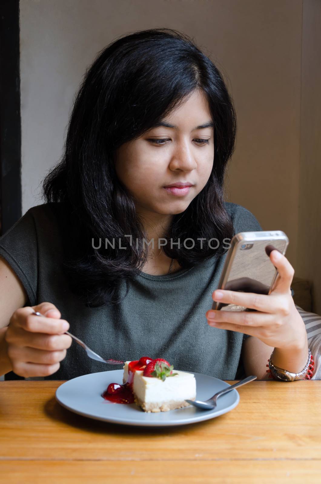 Young asian woman chating mobile phone with a cake in cafe