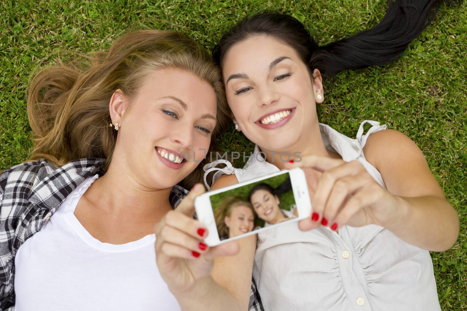Female best friends lying on the grass and taking selfies