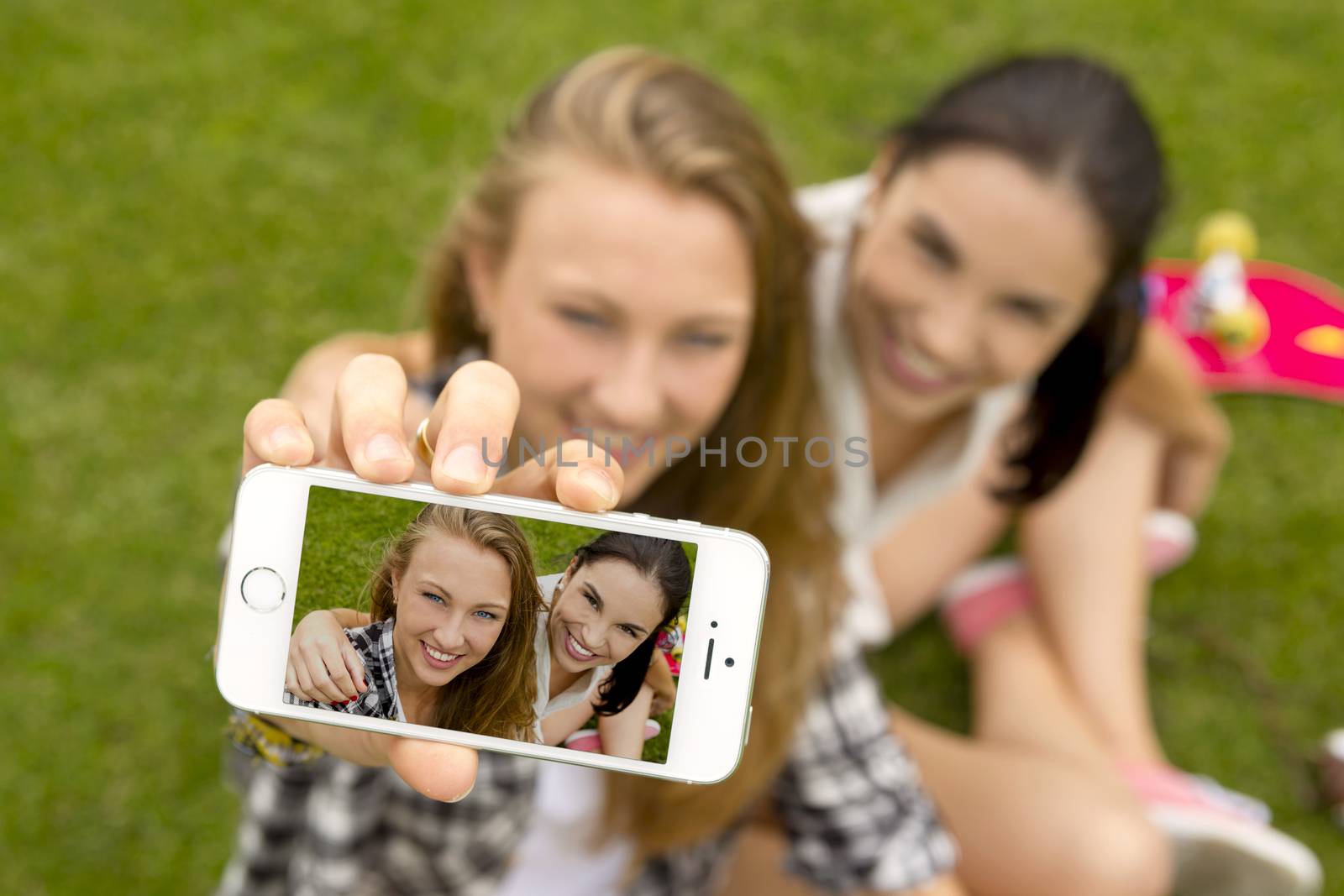 Female best friends lying on the grass and taking selfies