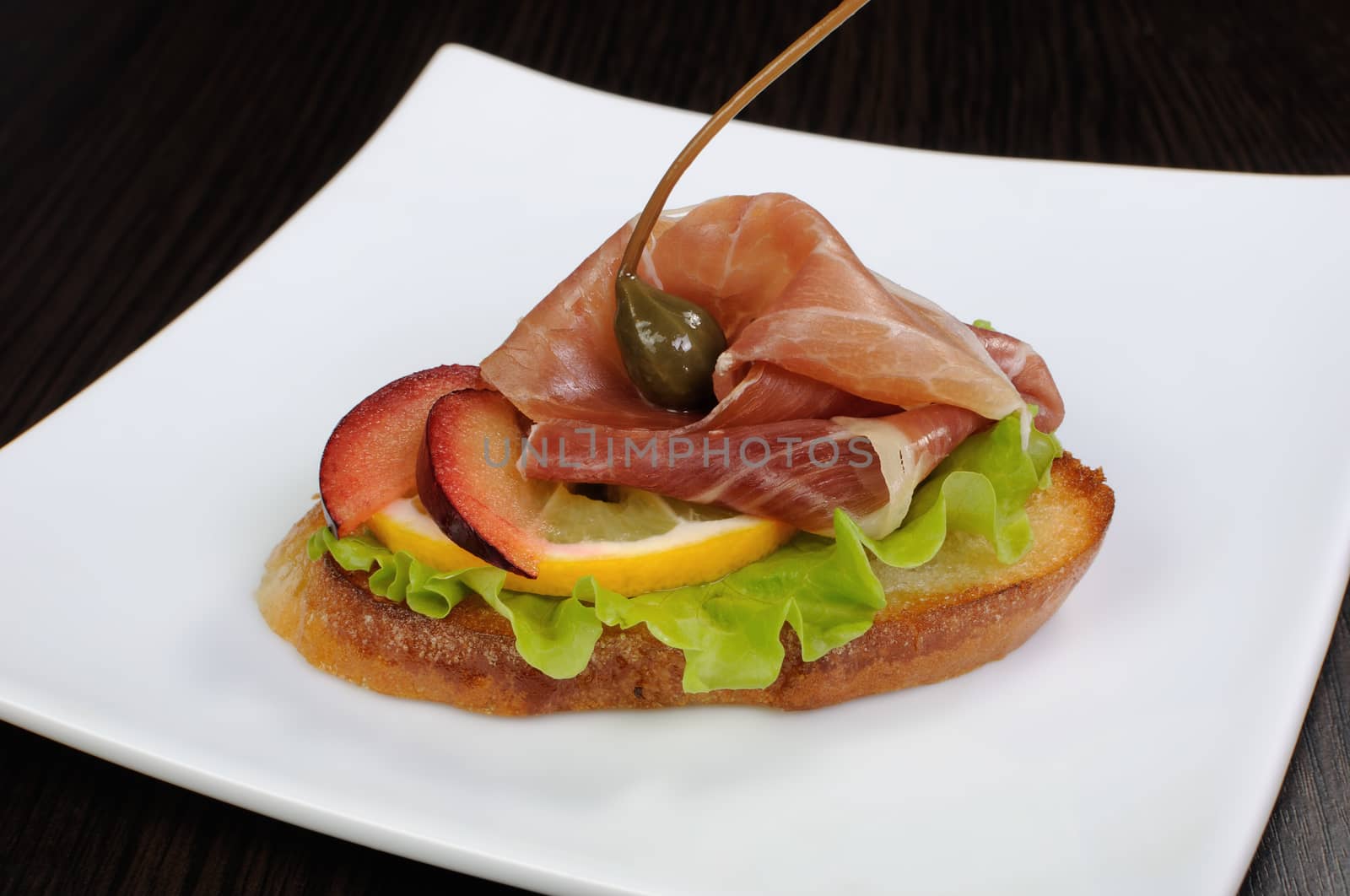 A slice of jamon on toast with lettuce, lemon, plum and capers