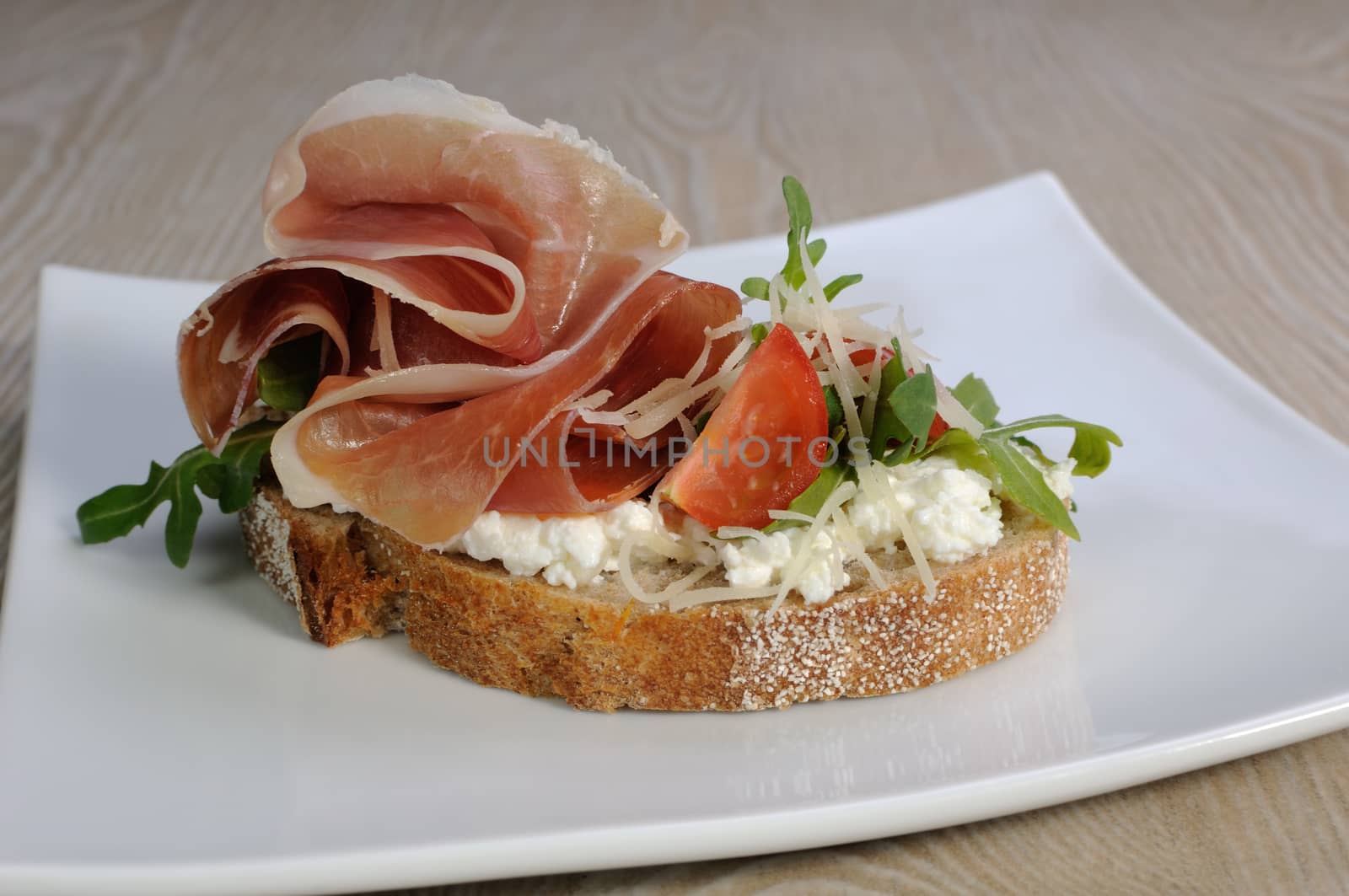 Sandwich of jamon with ricotta, arugula, cheese and a slice of cherry