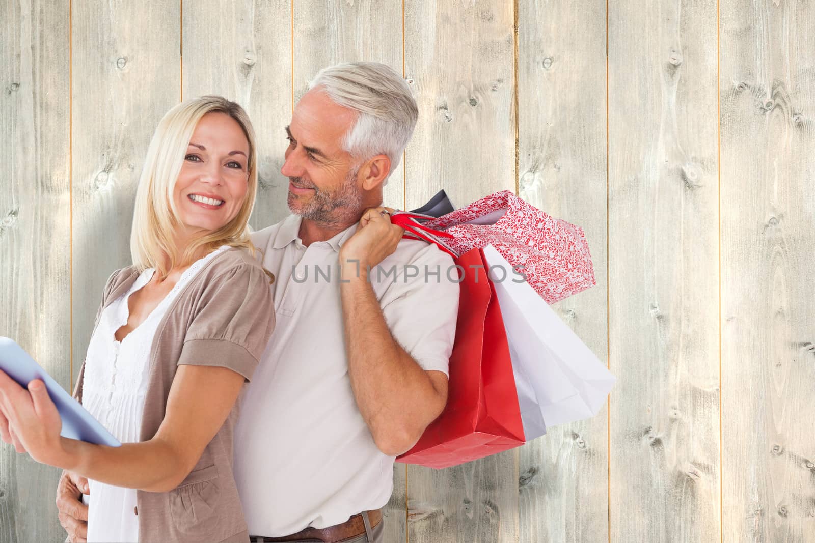 Happy couple with shopping bags and tablet pc against pale wooden planks