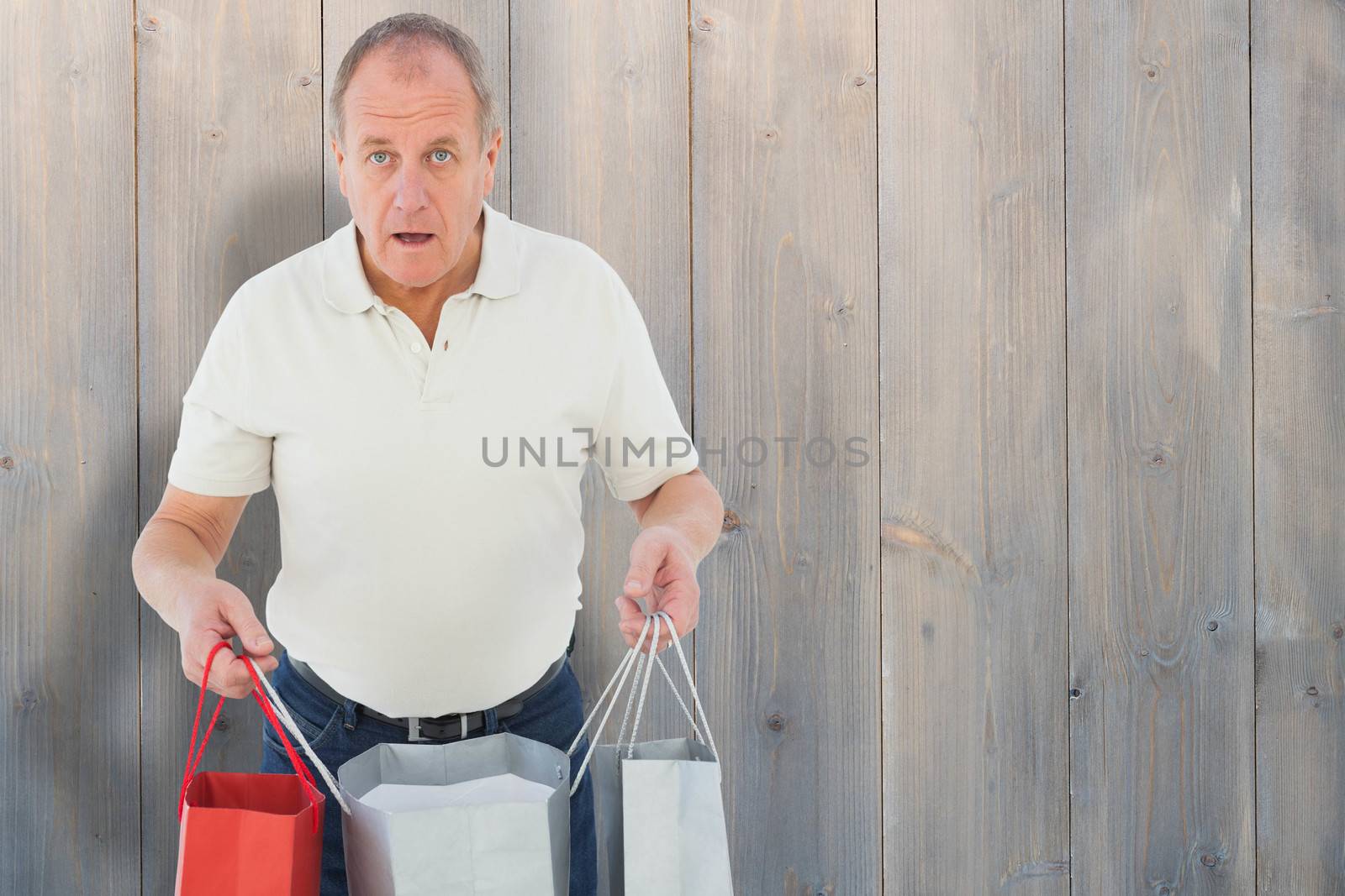 Shocked man holding shopping bags against pale grey wooden planks