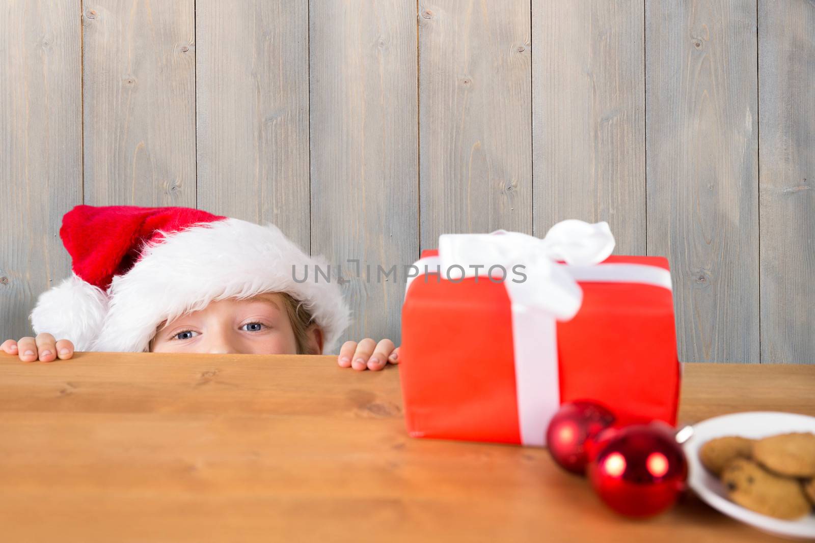 Festive boy peeking over table against pale grey wooden planks