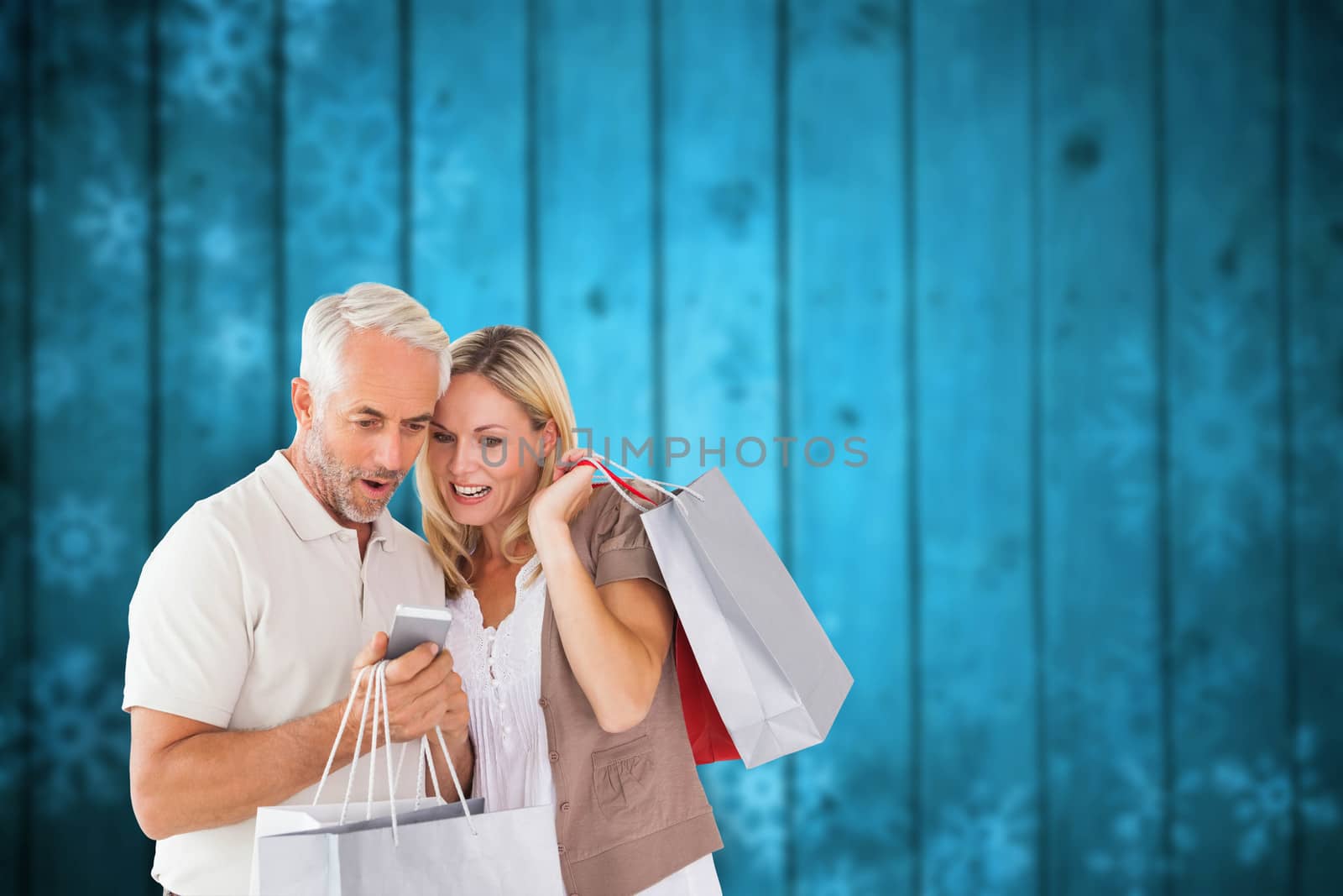 Happy couple with shopping bags and smartphone against blurred snowflakes on planks