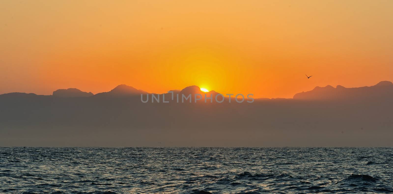 Orange sunrise at the ocean with mountains silhouettes 
