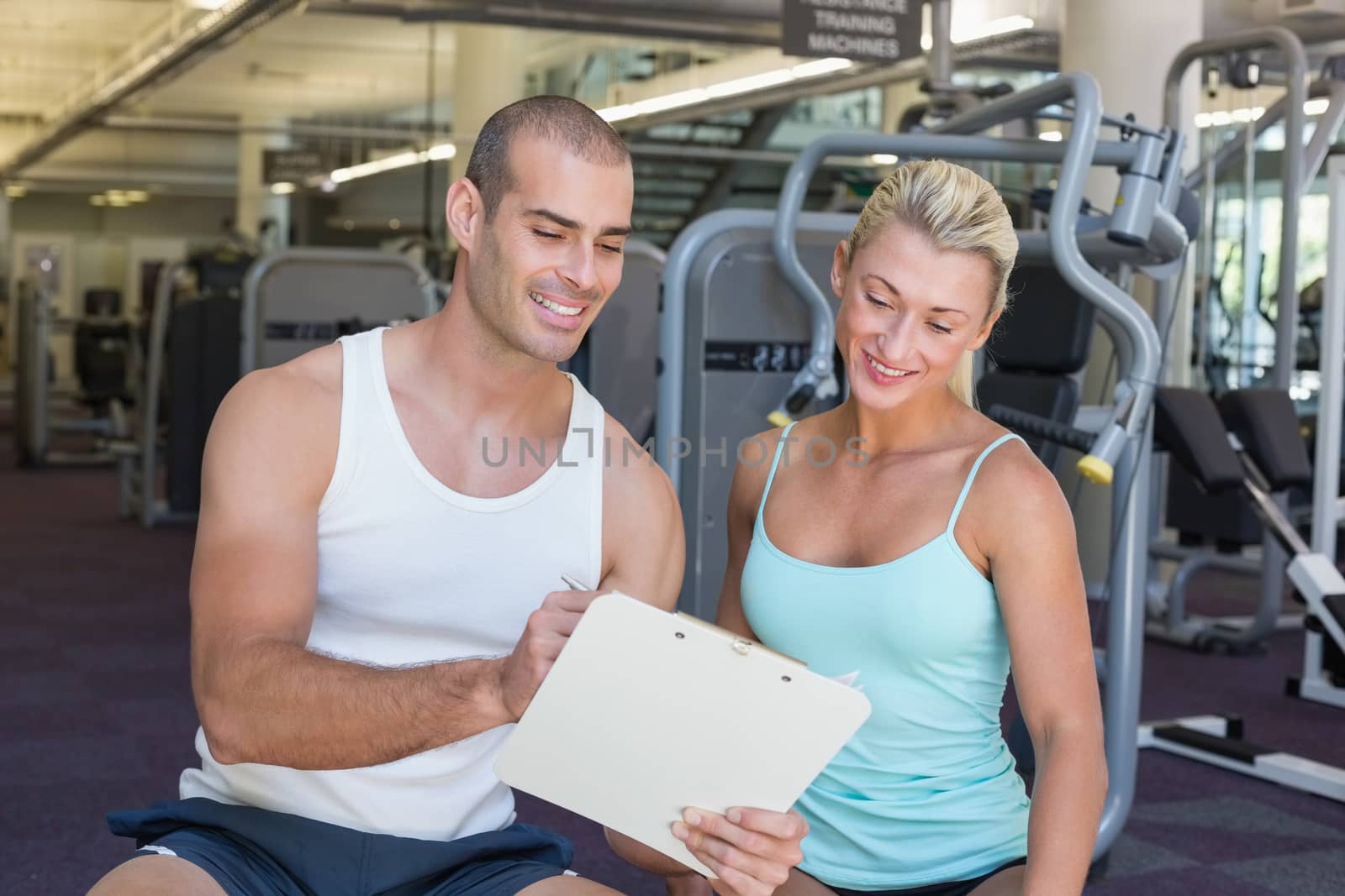 Beautiful young woman discussing her performance on clipboard with a trainer at the gym