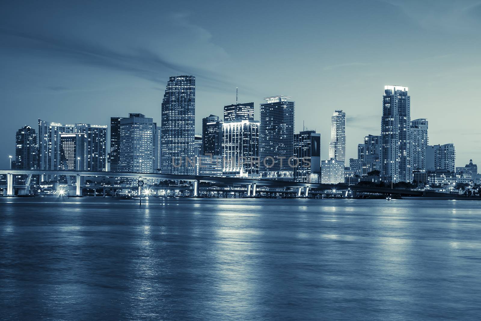 Miami skyline panorama at dusk with urban skyscrapers and bridge over sea with reflection 