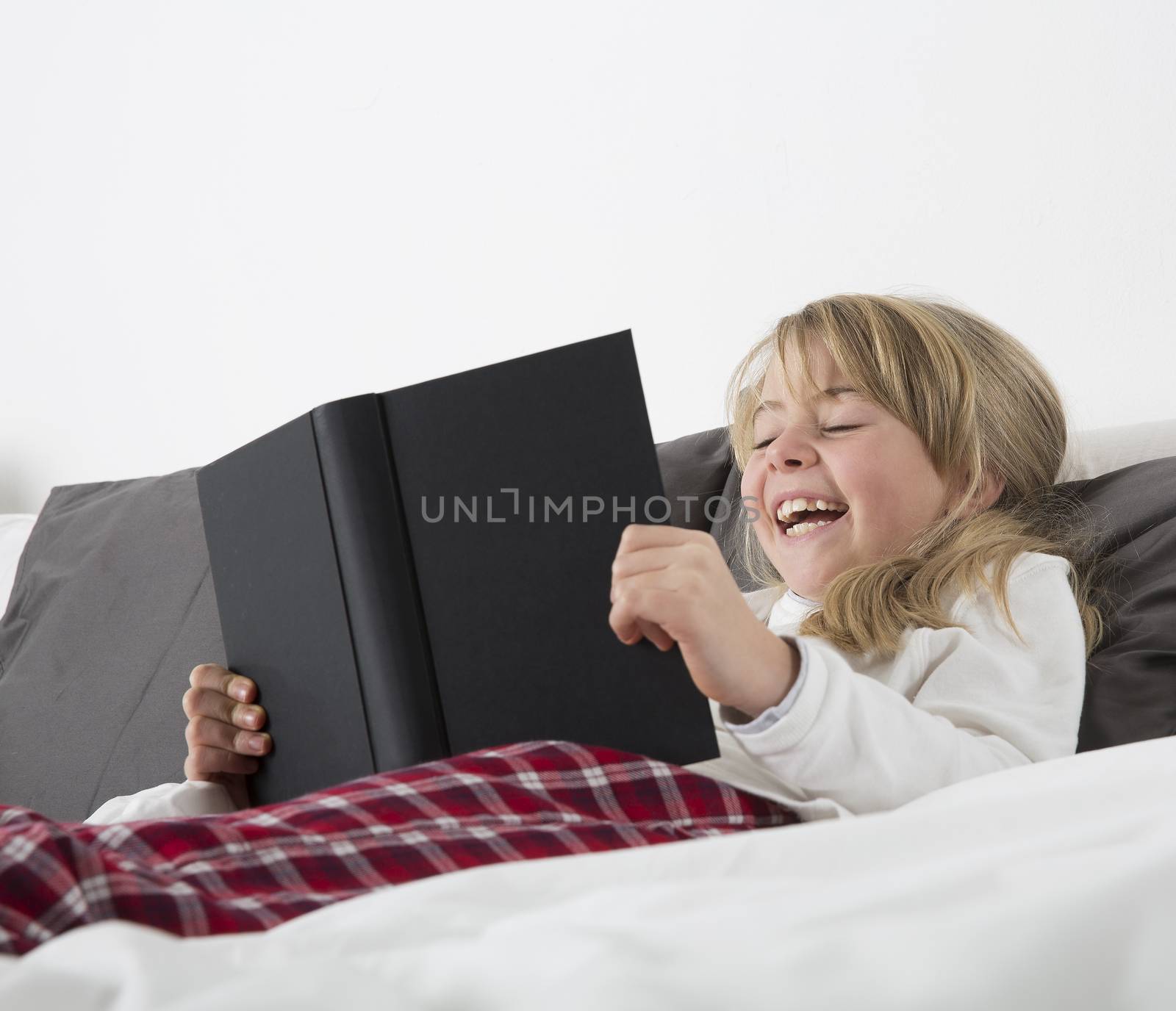 Laughing Young girl reading a book in bed