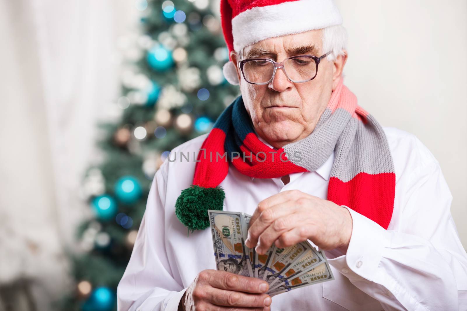 Senior man in Santa's hat holding money over Christmas background