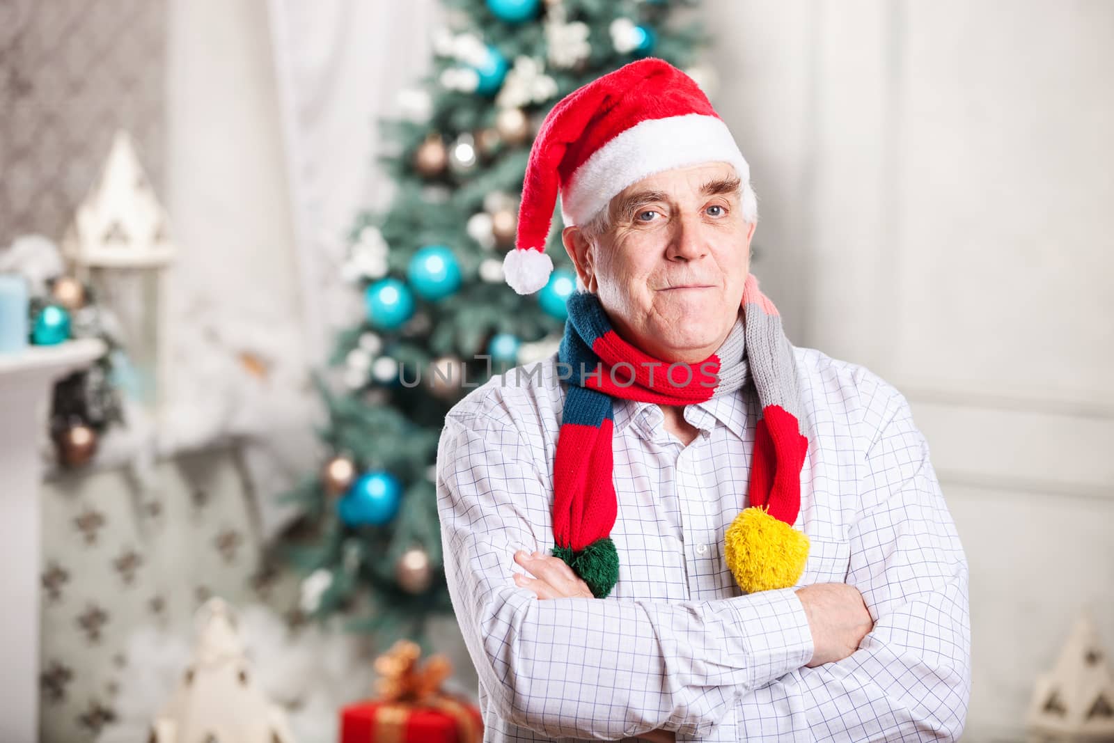 Portrait of mature man in Santa's hat and bright scarf standing with arms crossed over Christmas background